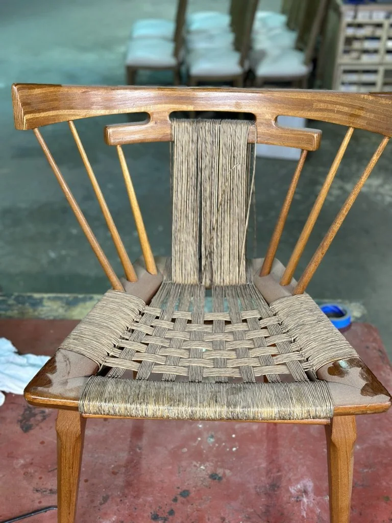 Wooden chair with a woven seat and backrest, placed on a red surface with a blurred background of chairs and outdoor setting.