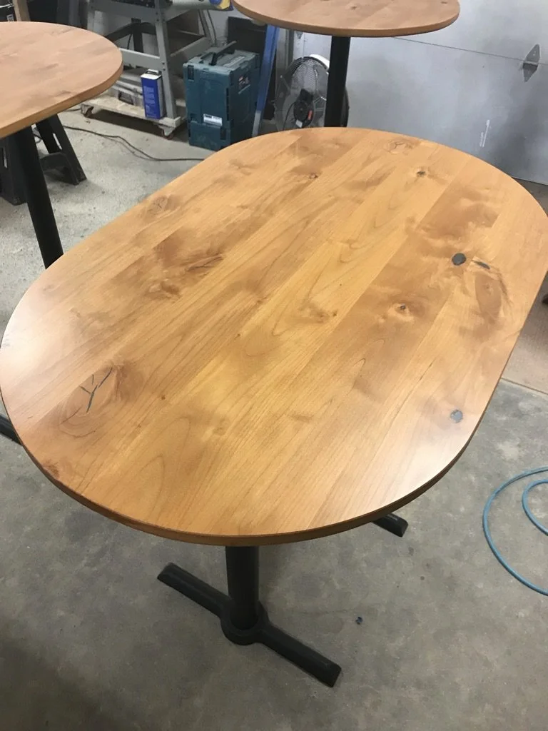 Wooden oval table with a black metal base in a workshop.