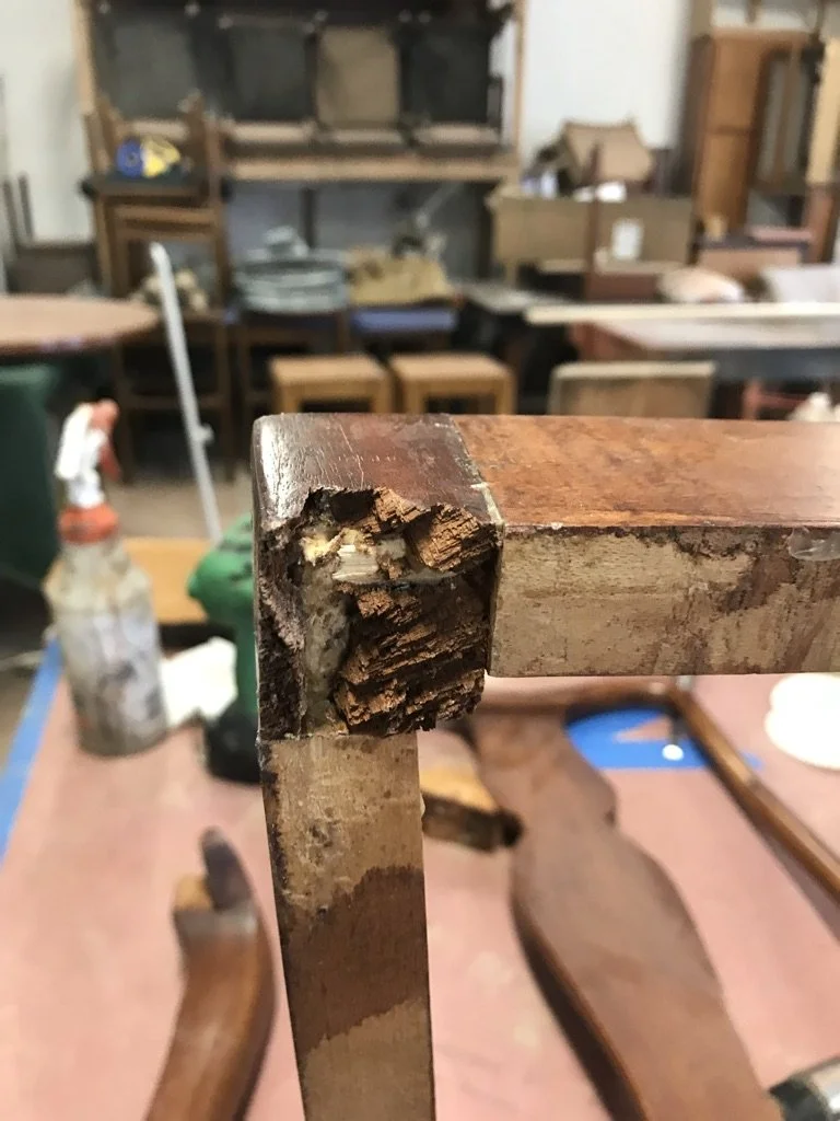 Close-up of a damaged wooden table corner showing rot and wood deterioration.