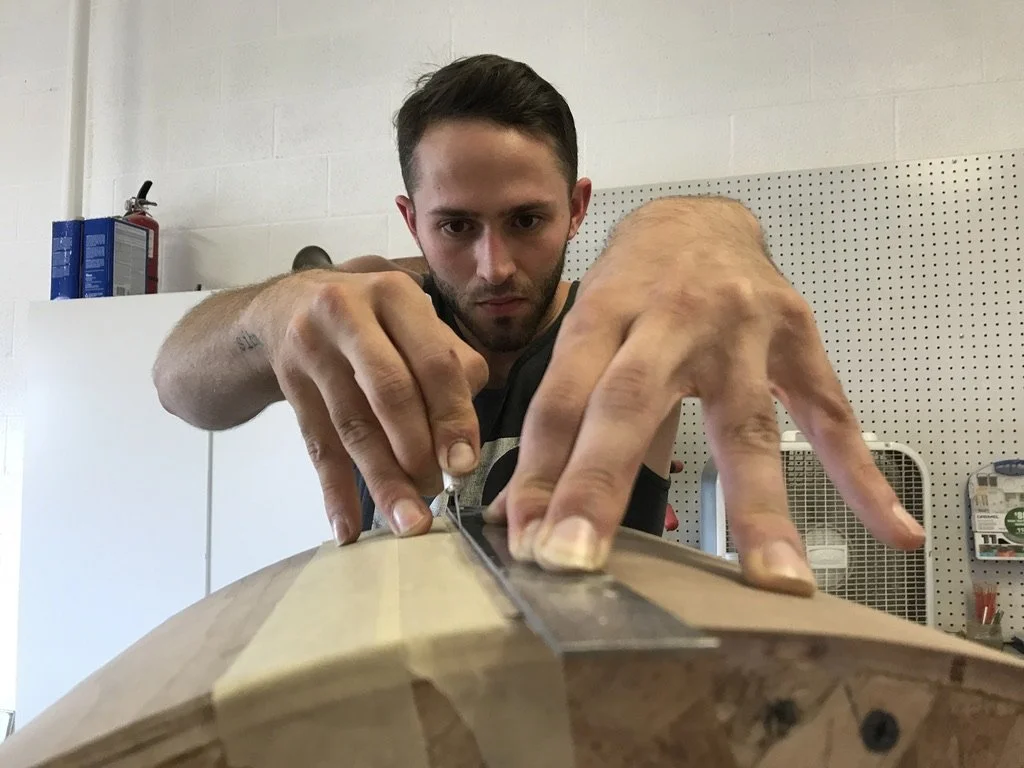 Young man working on a woodworking project, using a tool to shape or smooth a piece of wood.