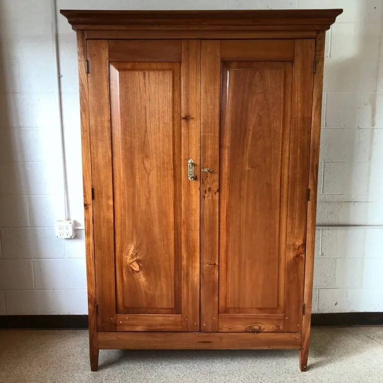 A wooden wardrobe with two doors, standing against a wall with a power outlet nearby.
