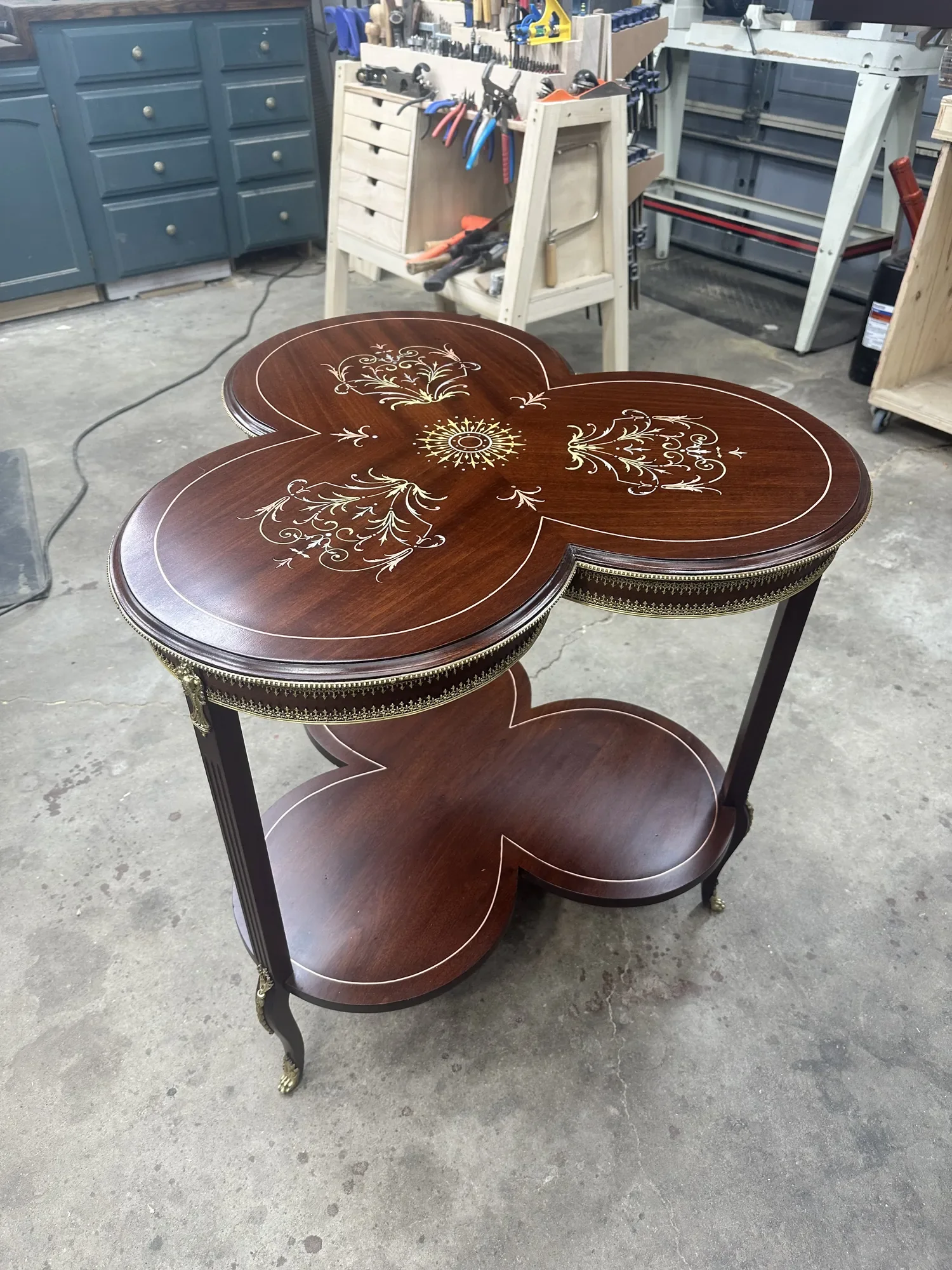 Restored Louis XVI–style trefoil guéridon in rich mahogany with a reattached brass gallery, fluted legs, and lower shelf