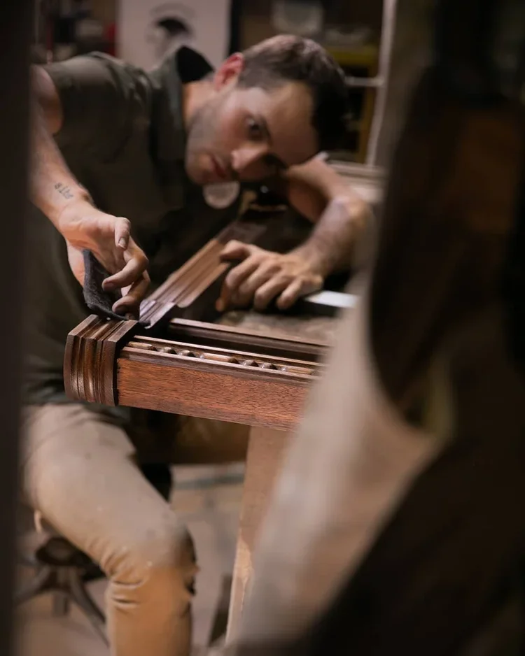 Man polishing a wooden piano keyboard in a workshop.
