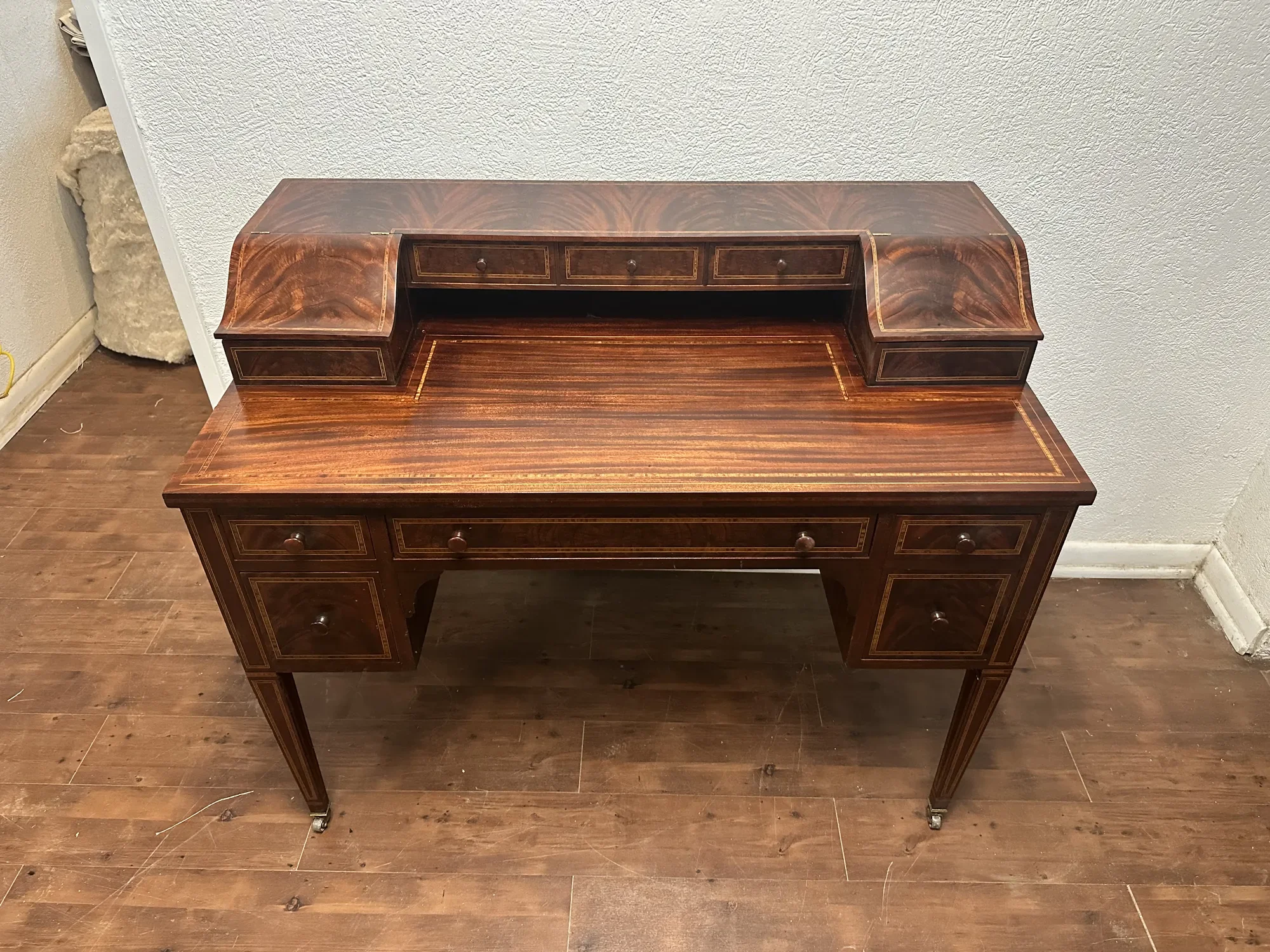 Sheraton-style flame mahogany writing desk with inlaid banding, a raised row of small drawers, and tapered legs on brass casters