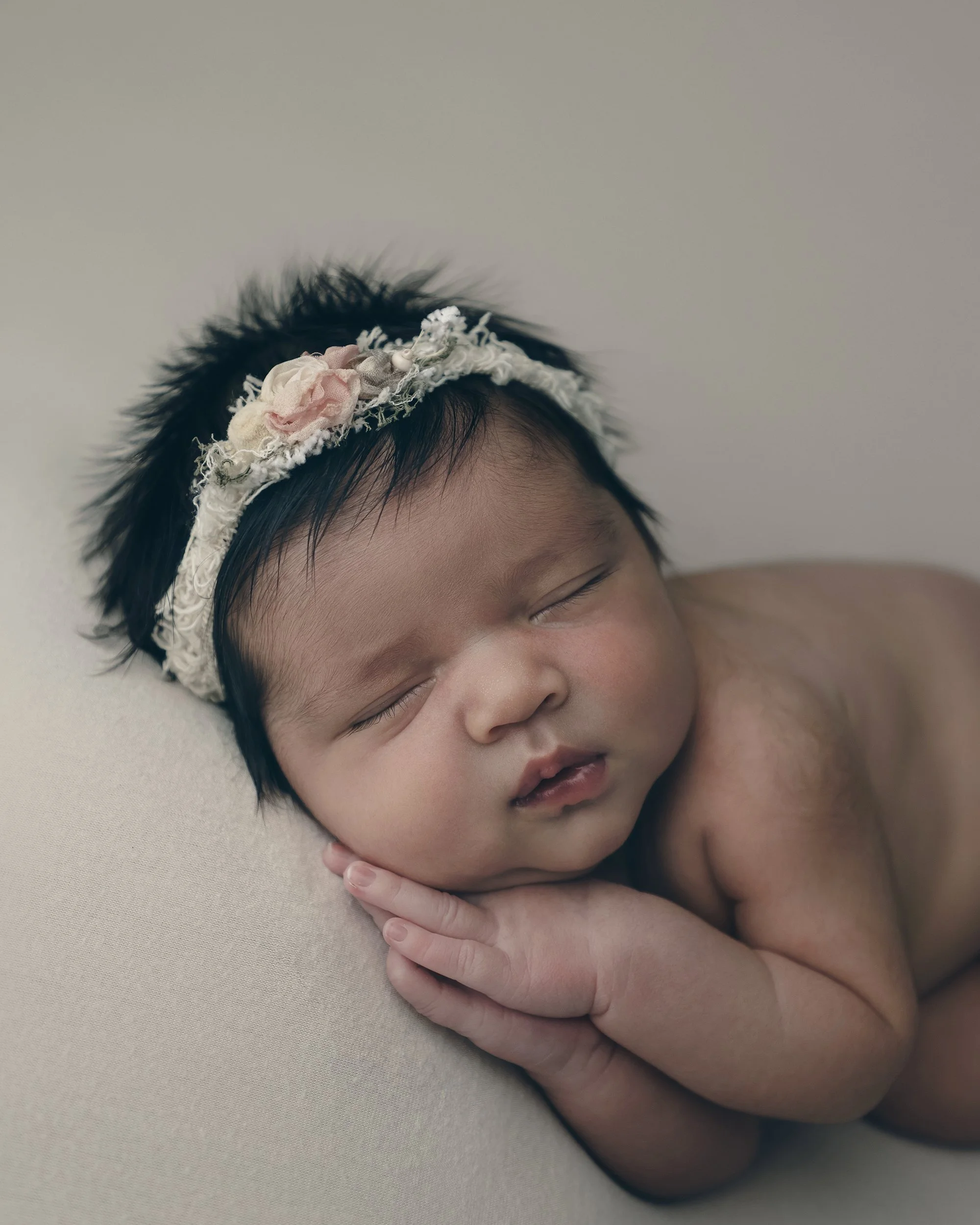 A sleeping baby with a floral headband, lying on a beige surface.