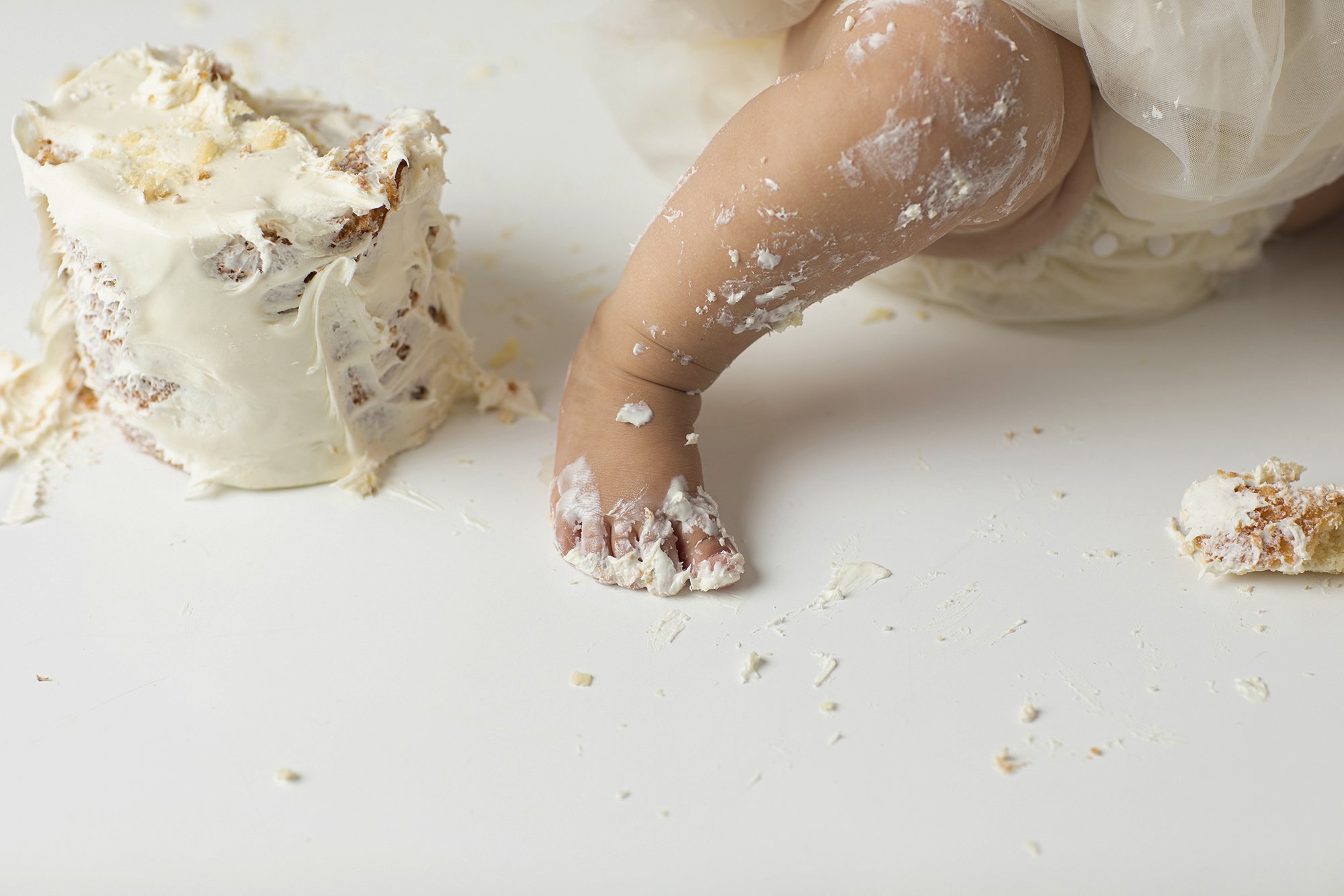 Child with a diaper on, playing in spilled white cake or frosting on a white surface.