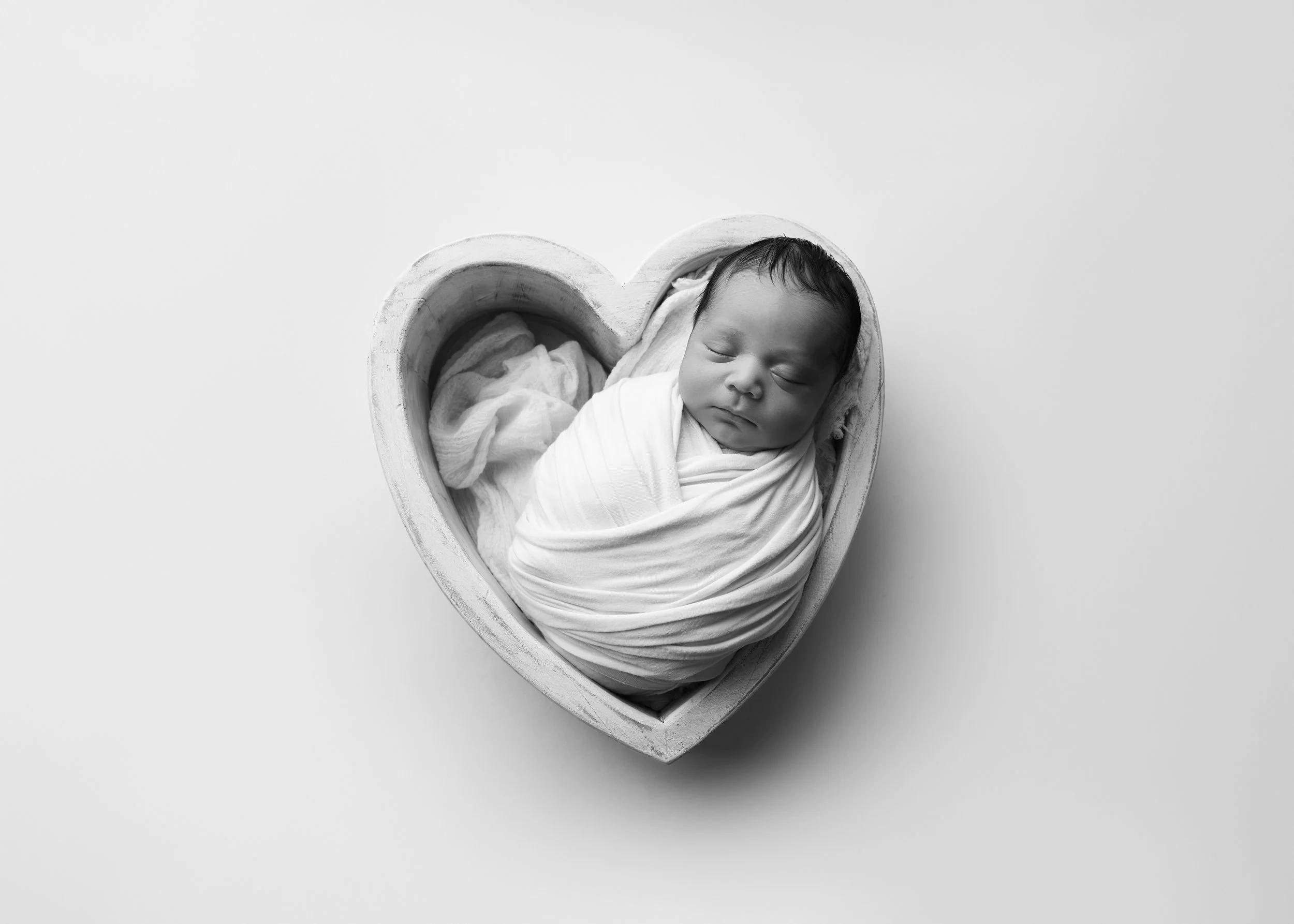 A sleeping baby wrapped in a blanket inside a heart-shaped box