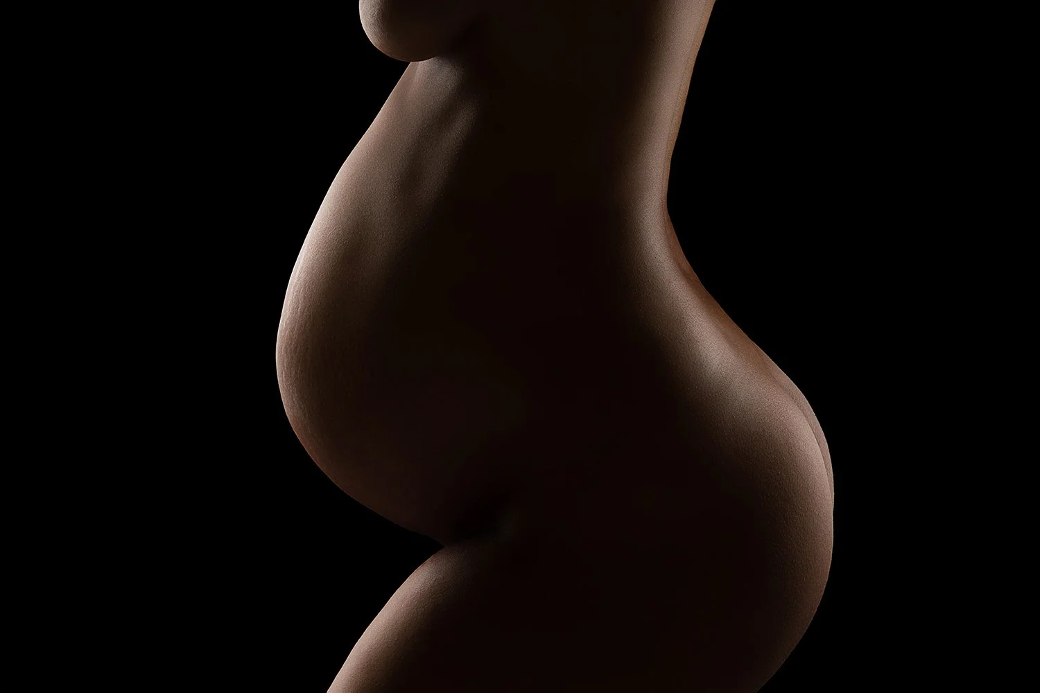 Close-up side view of a nude woman's torso and hips, with smooth skin against a black background.