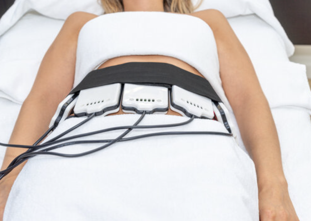 Person lying on a massage table table receiving a laser lipo session therapy with the laser lipo pads attached to their lower abdomen.