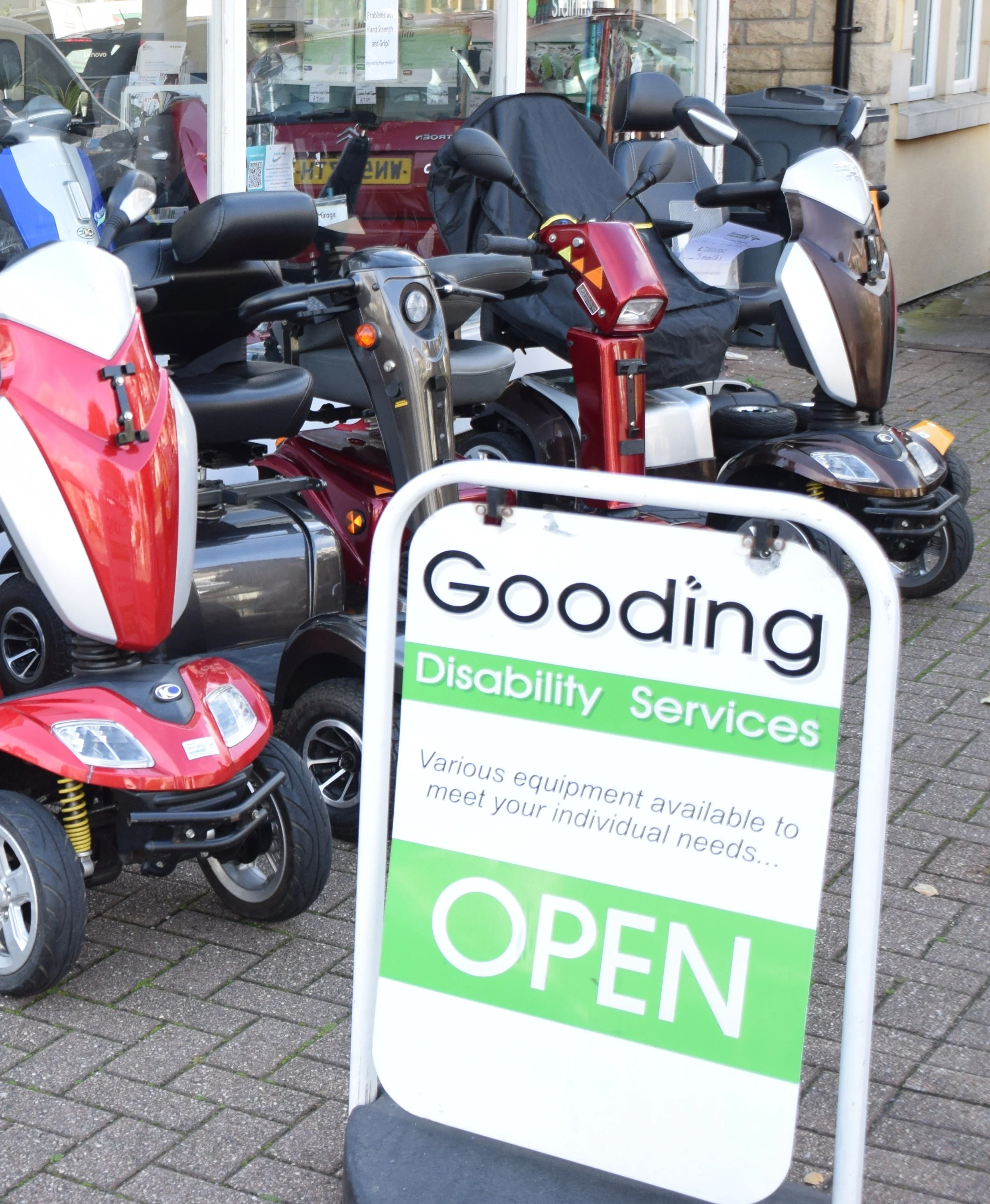 A stand with a sign for disability services outside a store, showing various mobility equipment including scooters and wheelchairs.
