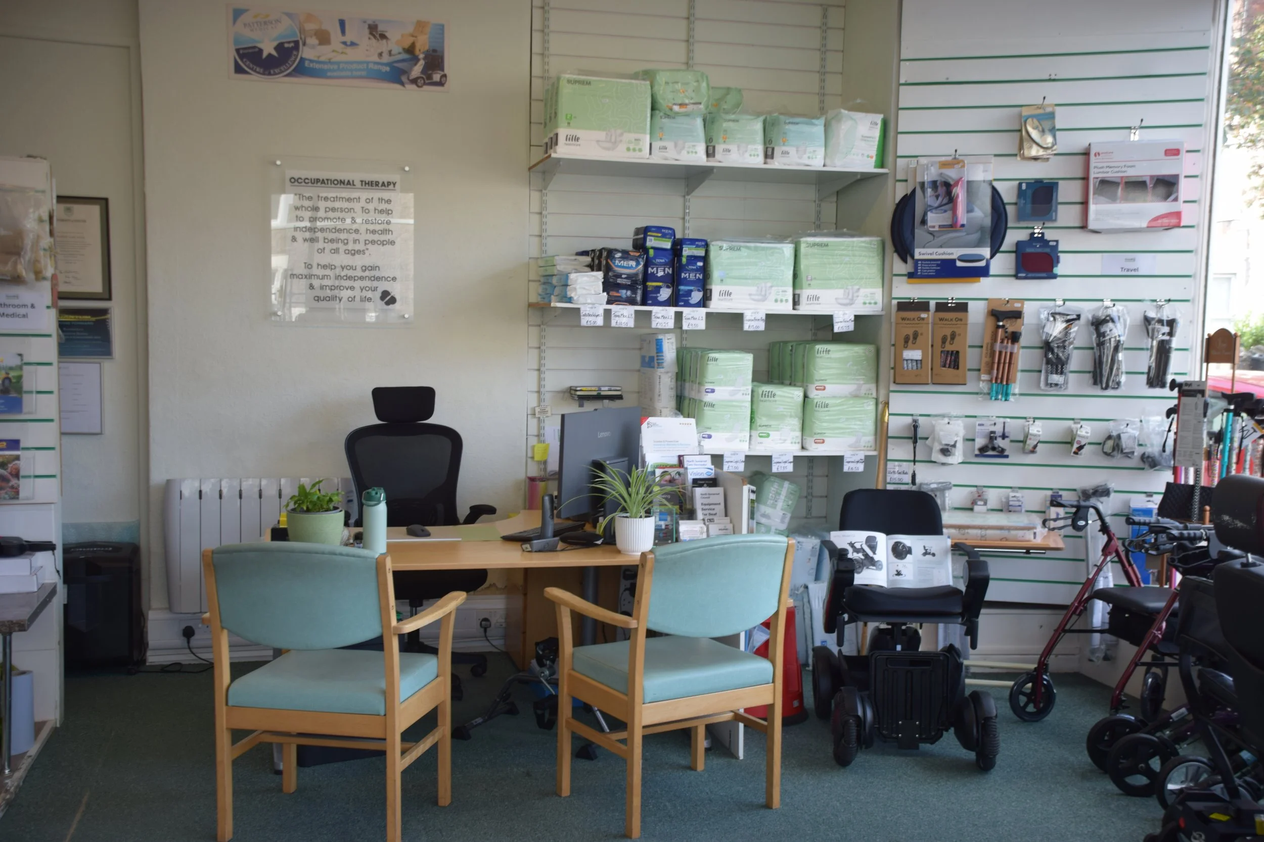 A medical supply store interior with shelves of adult diapers, wound care supplies, and healthcare products. There are chairs, a desk with a computer, and a variety of health and mobility aids visible.