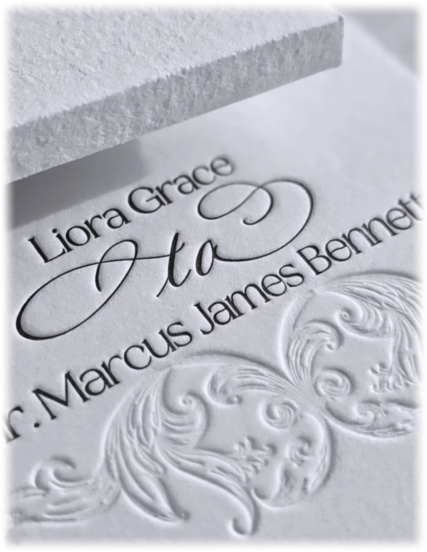 Close-up of an embossed wedding invitation with elegant black script, ornate scrollwork, and textured paper.