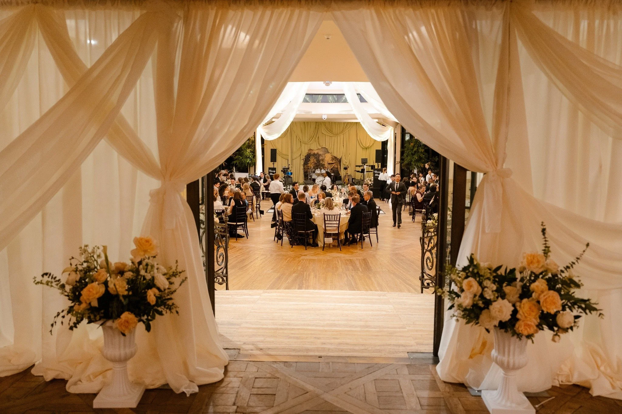 Elegant wedding reception hall viewed through a doorway draped with light-colored fabric and floral arrangements.