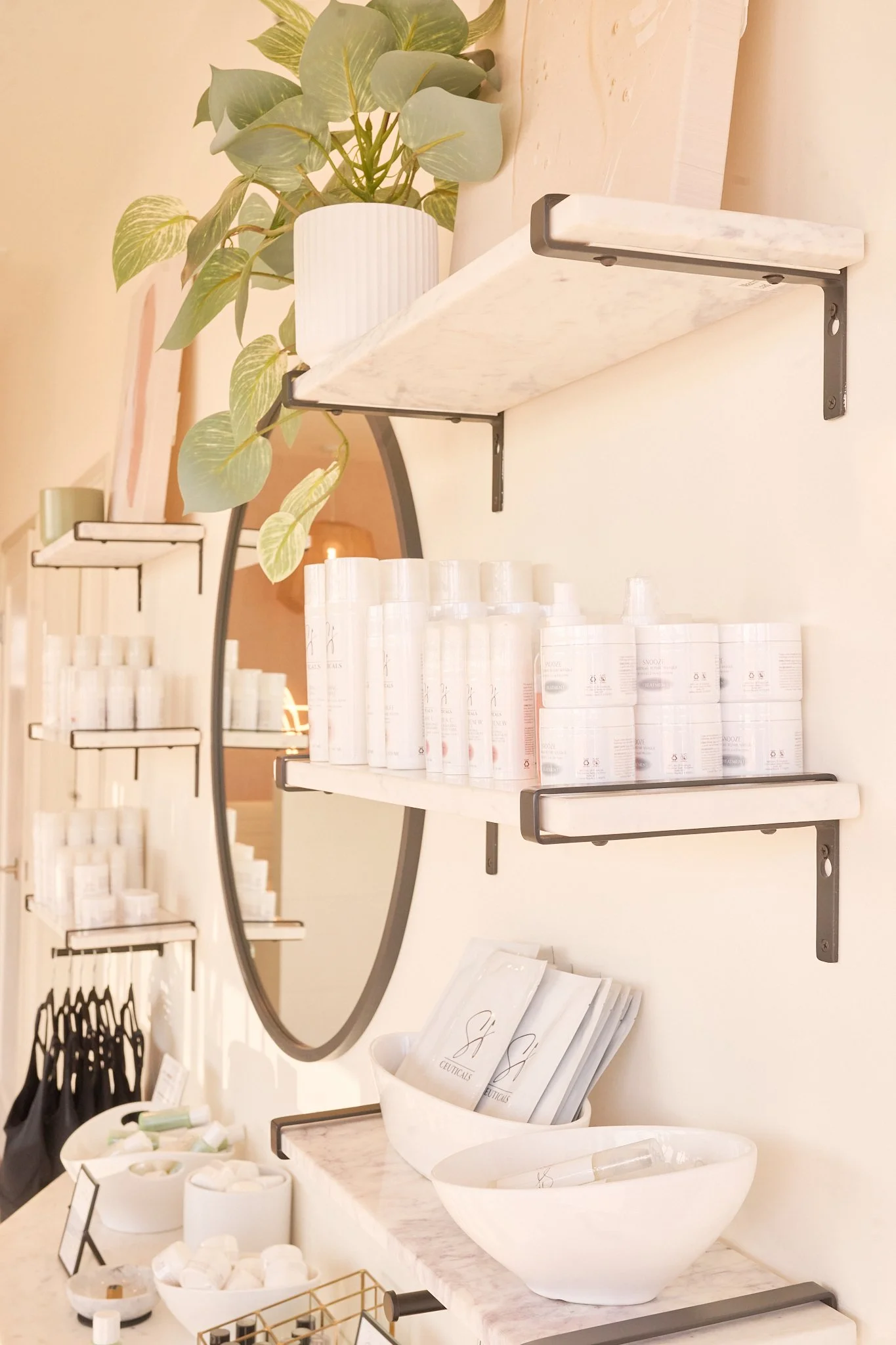 A retail display with shelves holding various skincare or beauty products, a potted plant, and a marble countertop with small containers and product packets.