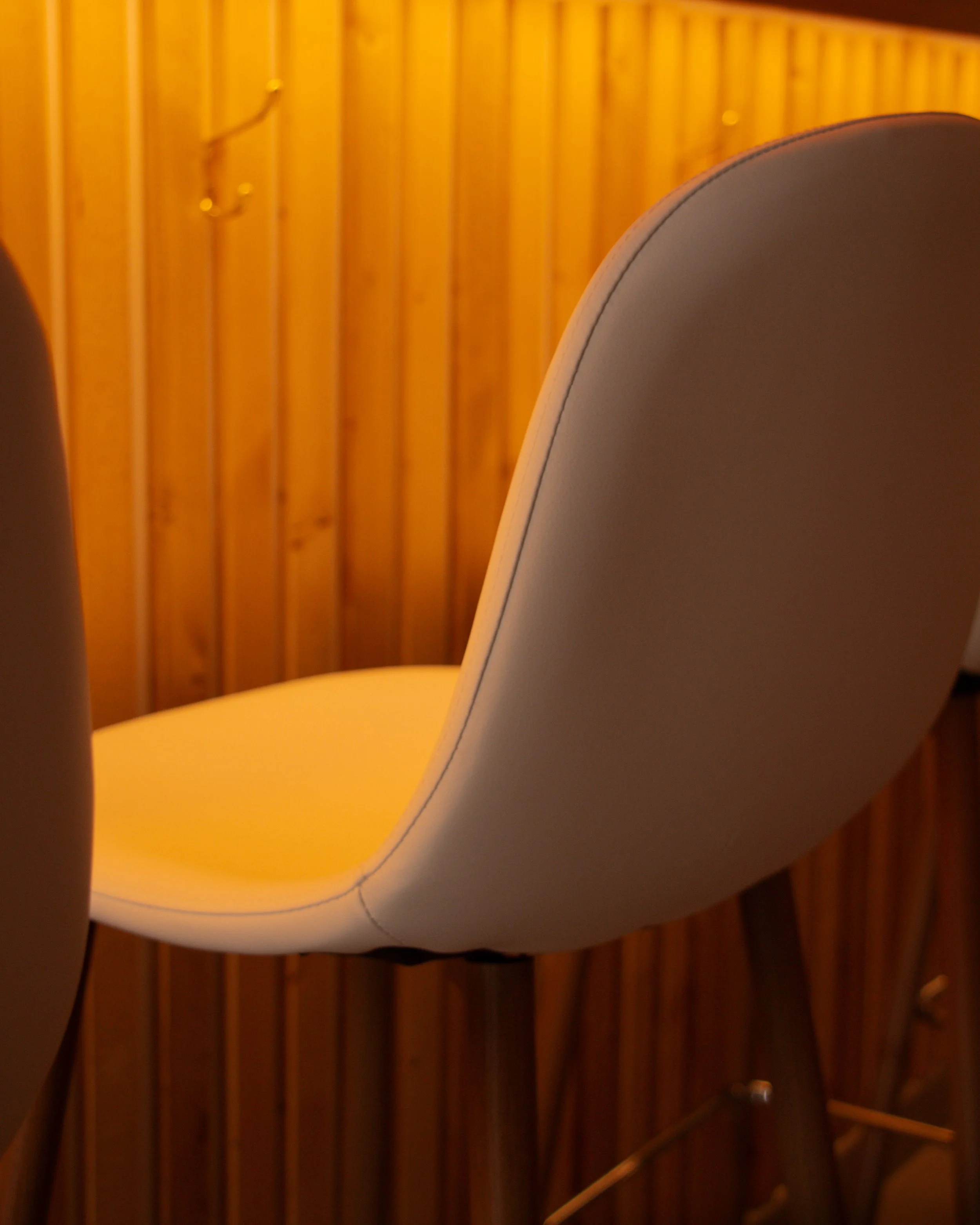 Close-up photo of a white, curved, modern lamp with warm orange lighting, mounted on a wooden wall with vertical panels.
