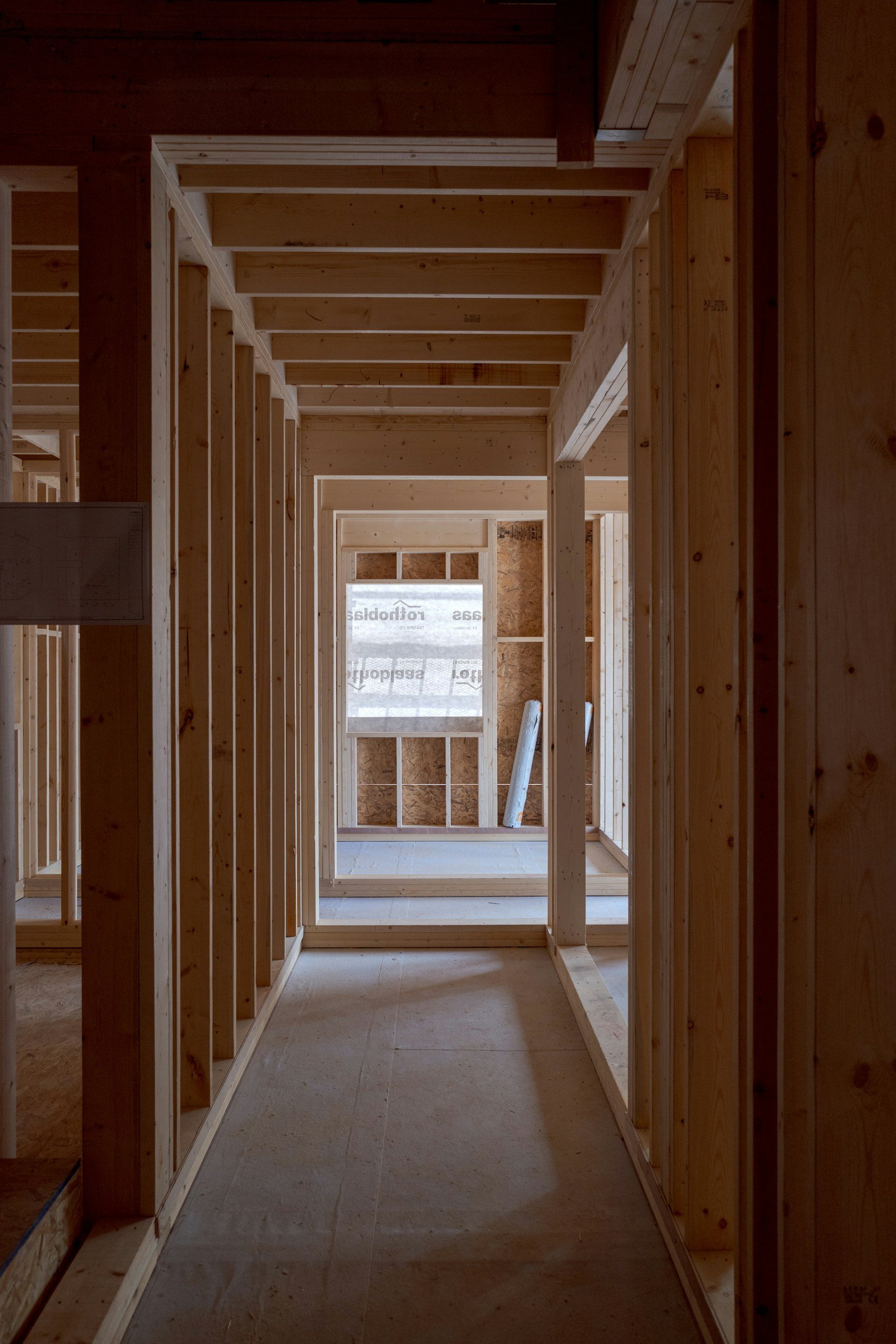 View of an unfinished wooden interior of a house under construction, showing framing and exposed walls with a window in the background.