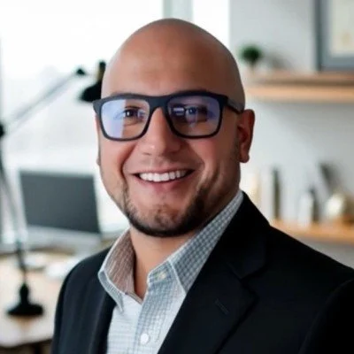 A smiling man with glasses wearing a suit in an office setting.