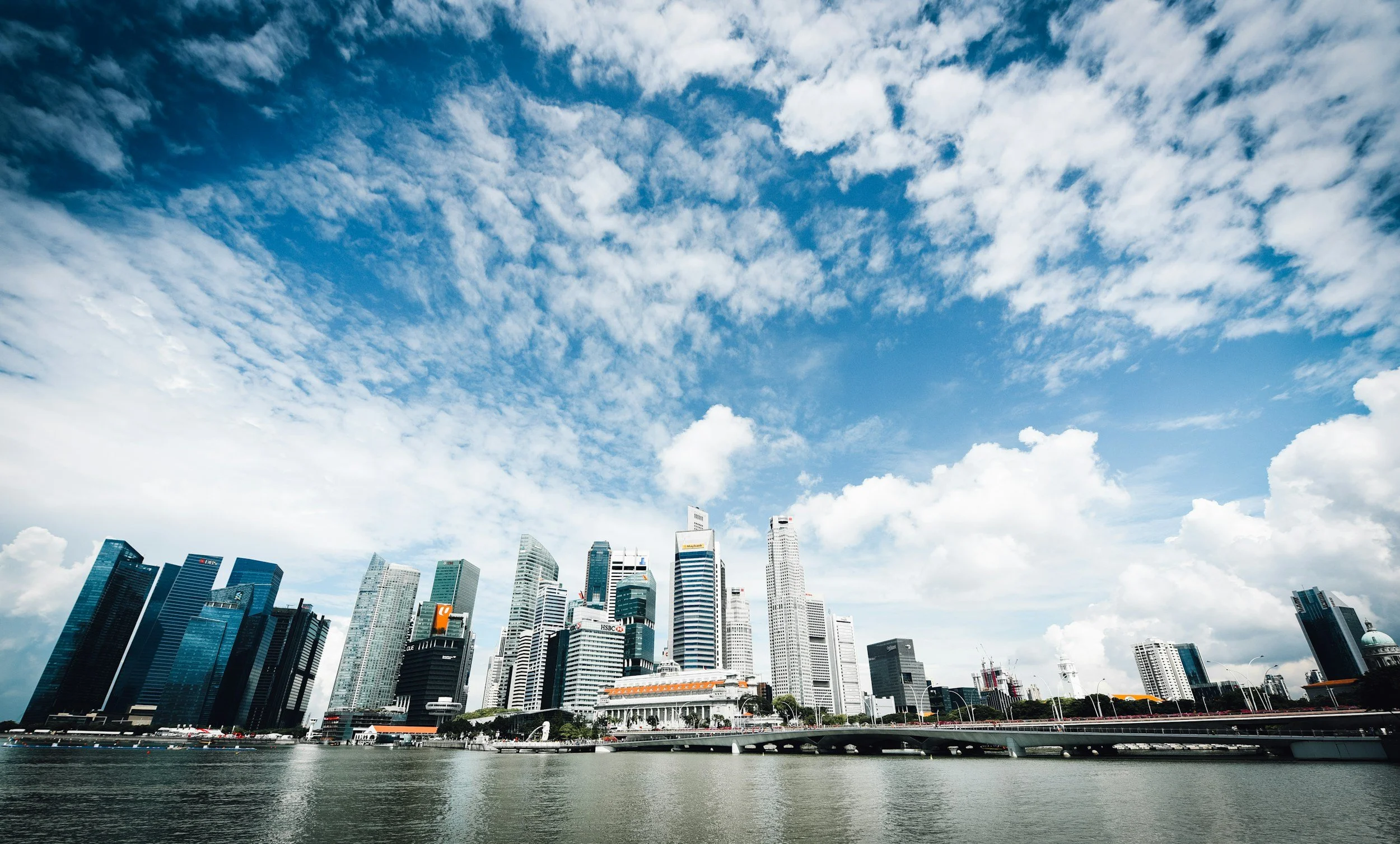 City skyline with tall skyscrapers along a waterfront under a partly cloudy blue sky