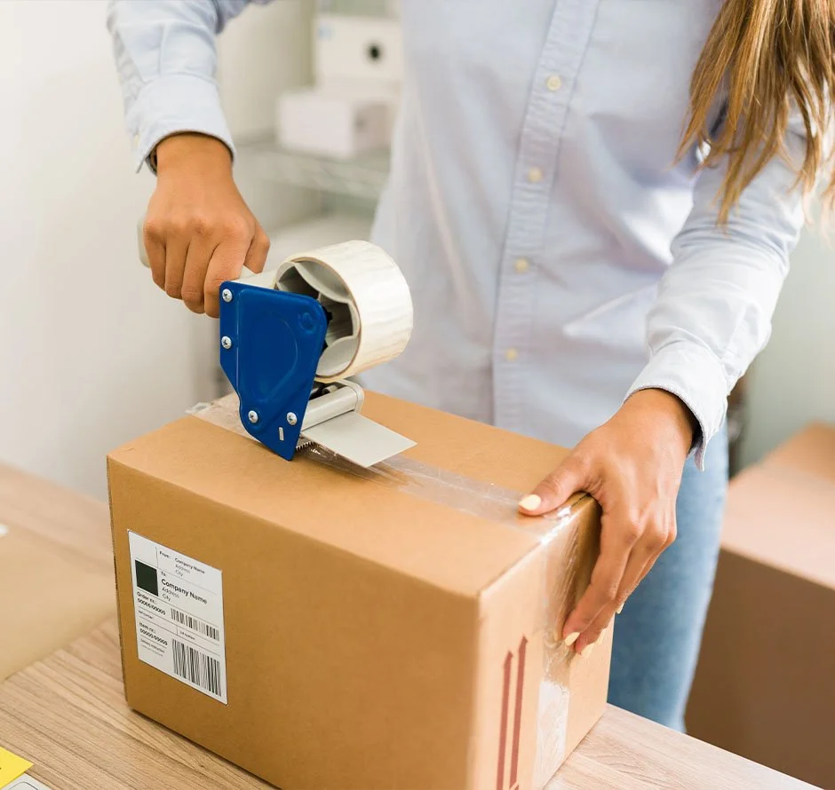 Person sealing a cardboard box with packing tape using a tape dispenser.