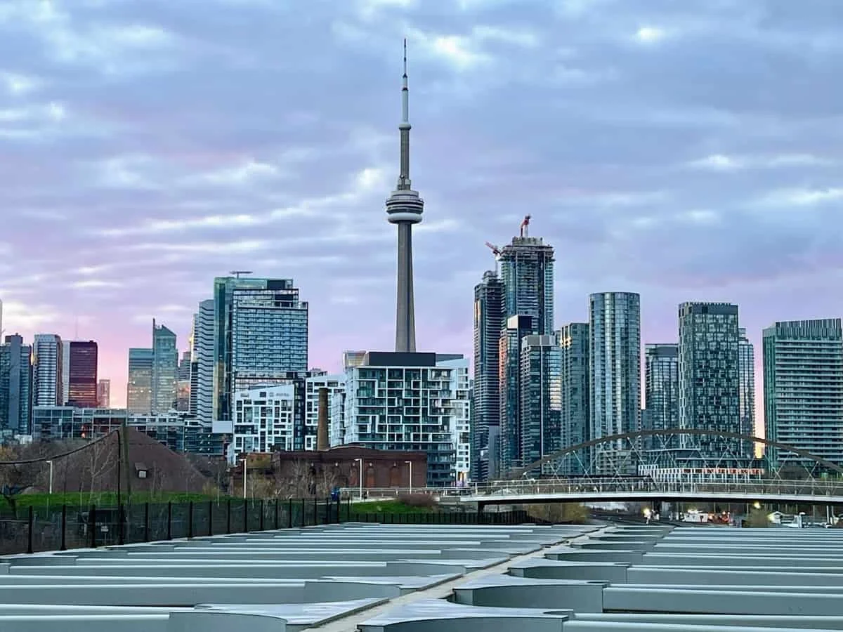 Toronto skyline featuring the CN Tower and surrounding high-rise buildings under cloudy sky.