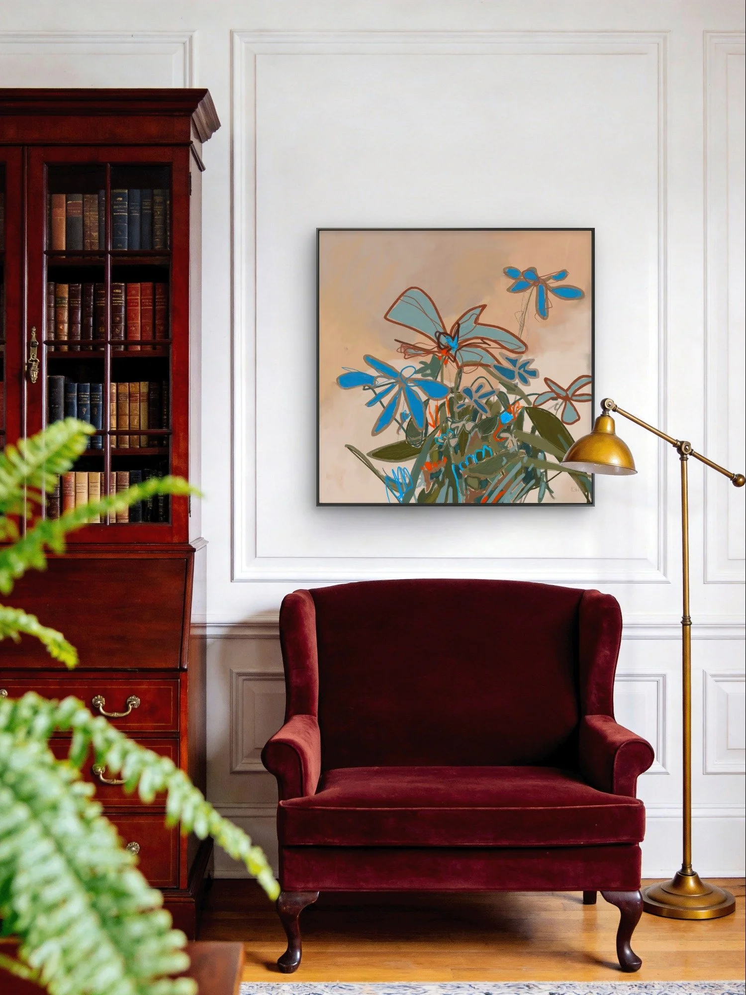 ''In Full Feeling,' a contemporary abstract botanical print hangs above a vintage red velvet armchair in a room with white paneled walls, a gold floor lamp, and a wooden bookshelf filled with books.