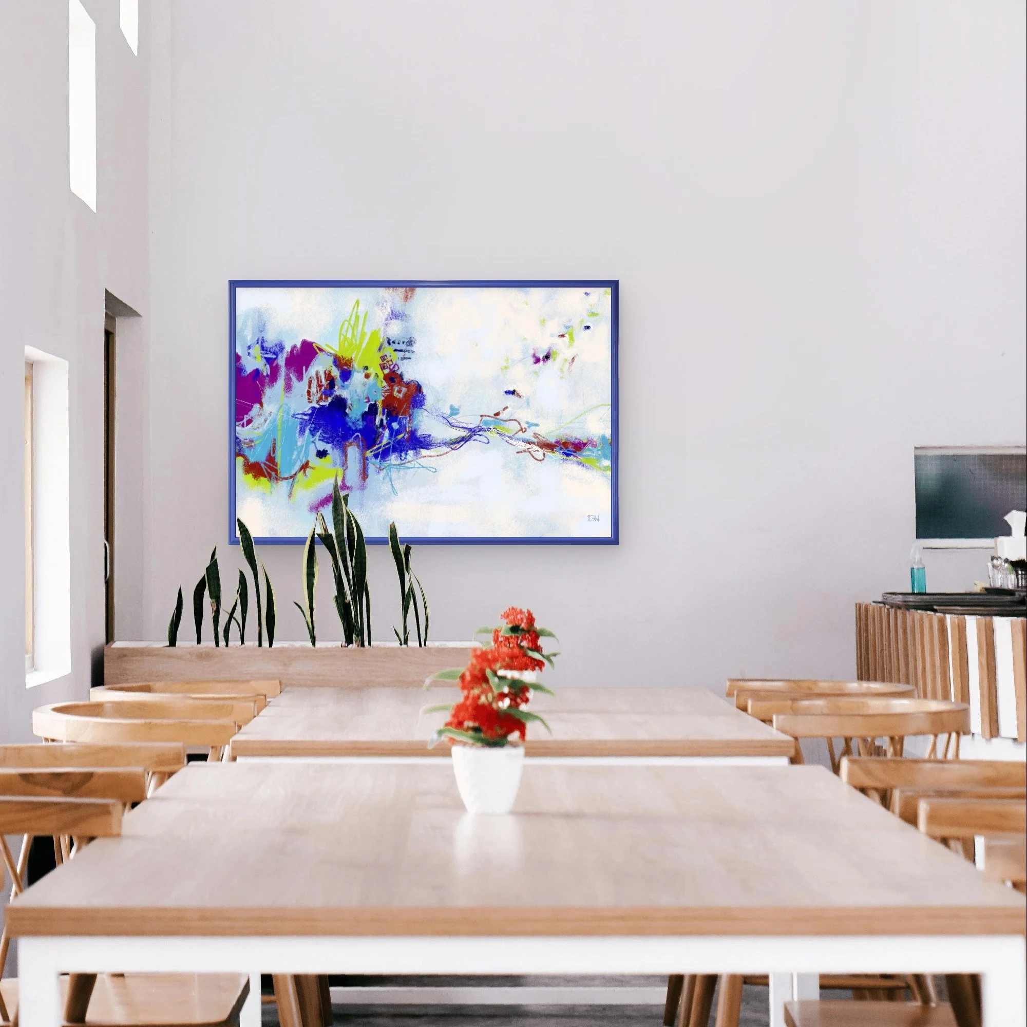 A modern restaurant with a long wooden table, surrounded by matching chairs, and a colorful abstract painting called 'All We Have Is Now' by Emily Whitish hangs on the white wall behind the table.