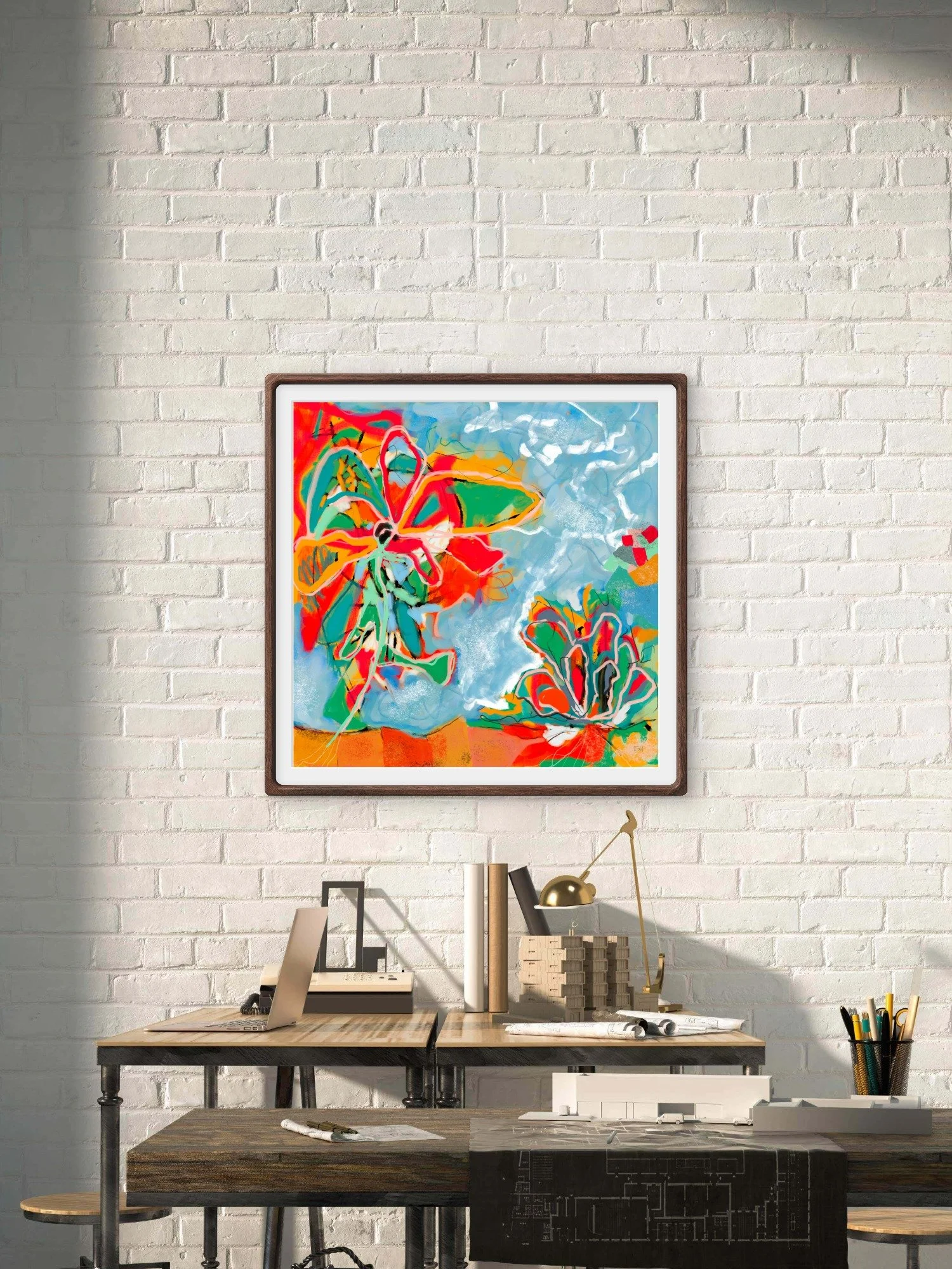 'Caught Fire,' a colorful abstract painting with bright colors like red, orange, yellow, green, blue, and black, hangs on a white brick wall above a workspace with various office supplies. The artist is Emily Whitish of Bainbridge Island, WA.