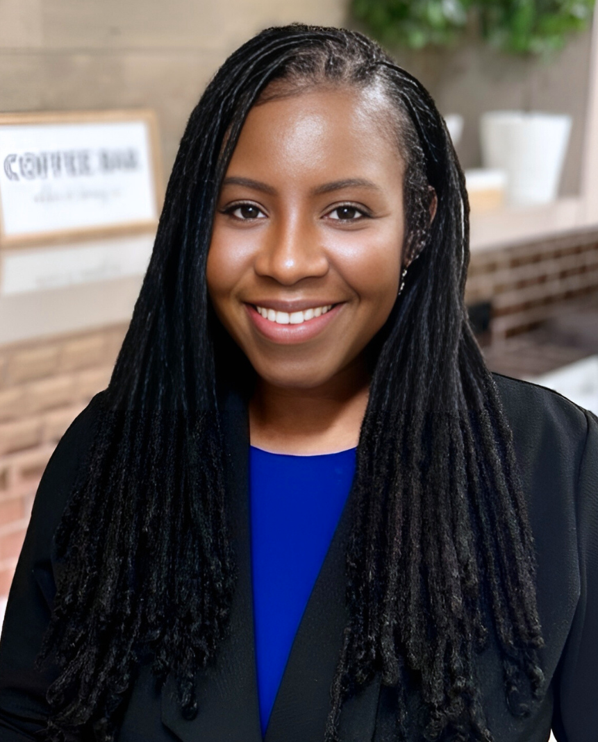 Photo of Dr. Darlene M. Scott with long black dreadlocks, smiling, wearing a black blazer over a blue top, in an indoor setting with a blurred background.