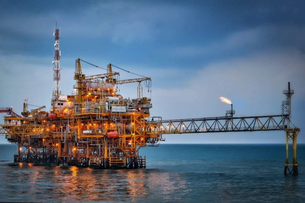 Oil platform in the ocean with a lit flare stack and a cloudy sky.