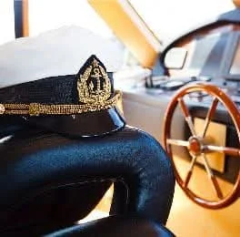 A captain's hat resting on a car seat with a ship's wheel in the background.
