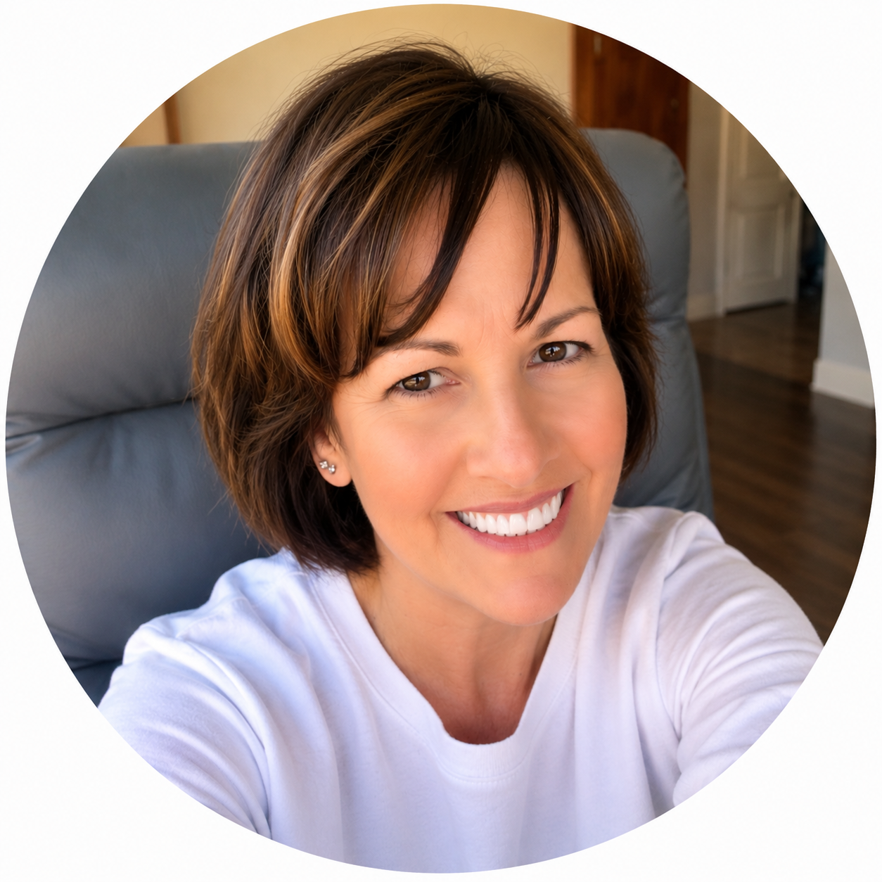Smiling woman with short brown hair and earrings taking a selfie indoors.