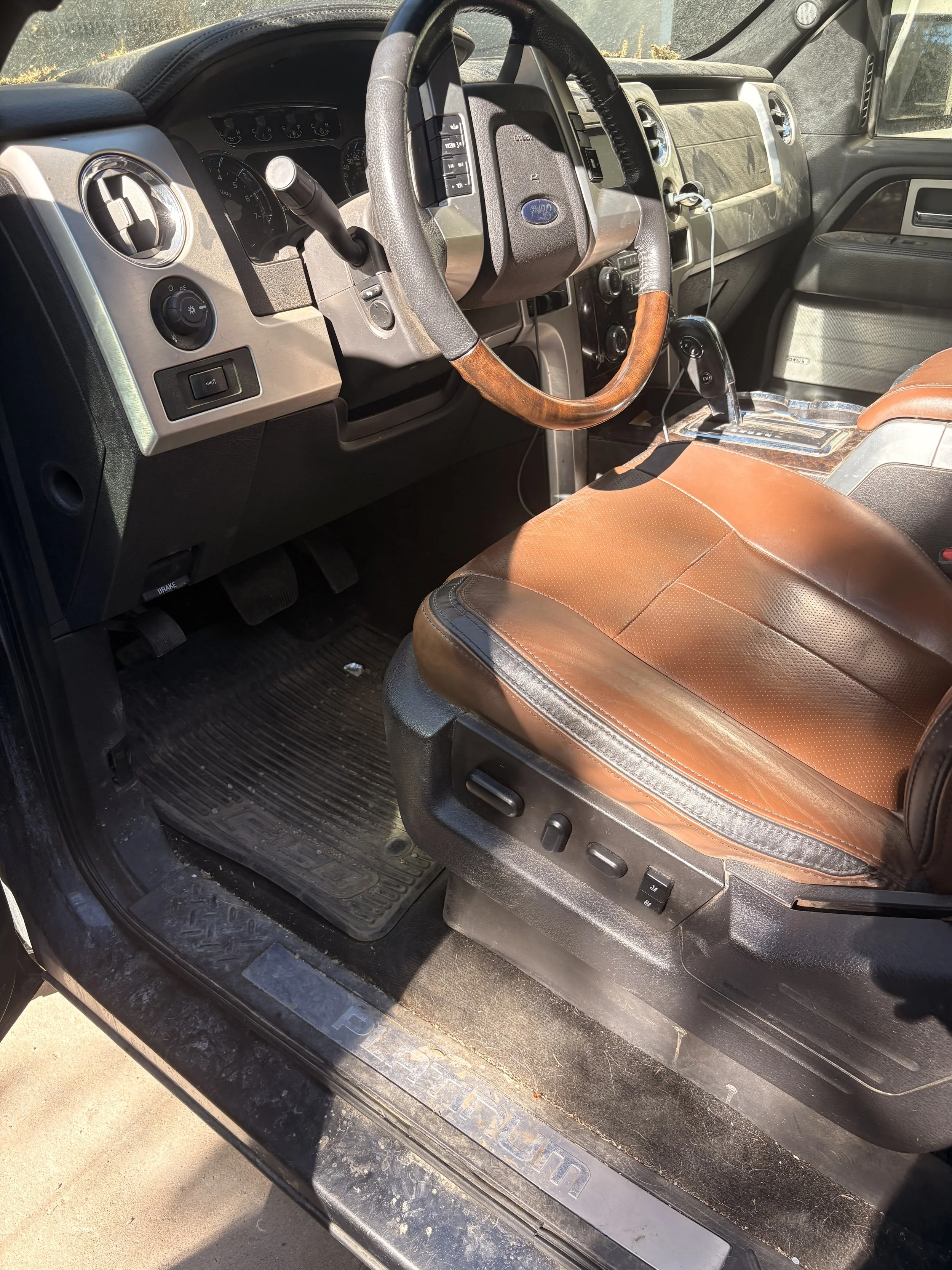 Interior of a vehicle with a brown leather seat, dashboard, steering wheel, gear shift, and a key inserted into the ignition, viewed from the open driver's side door.