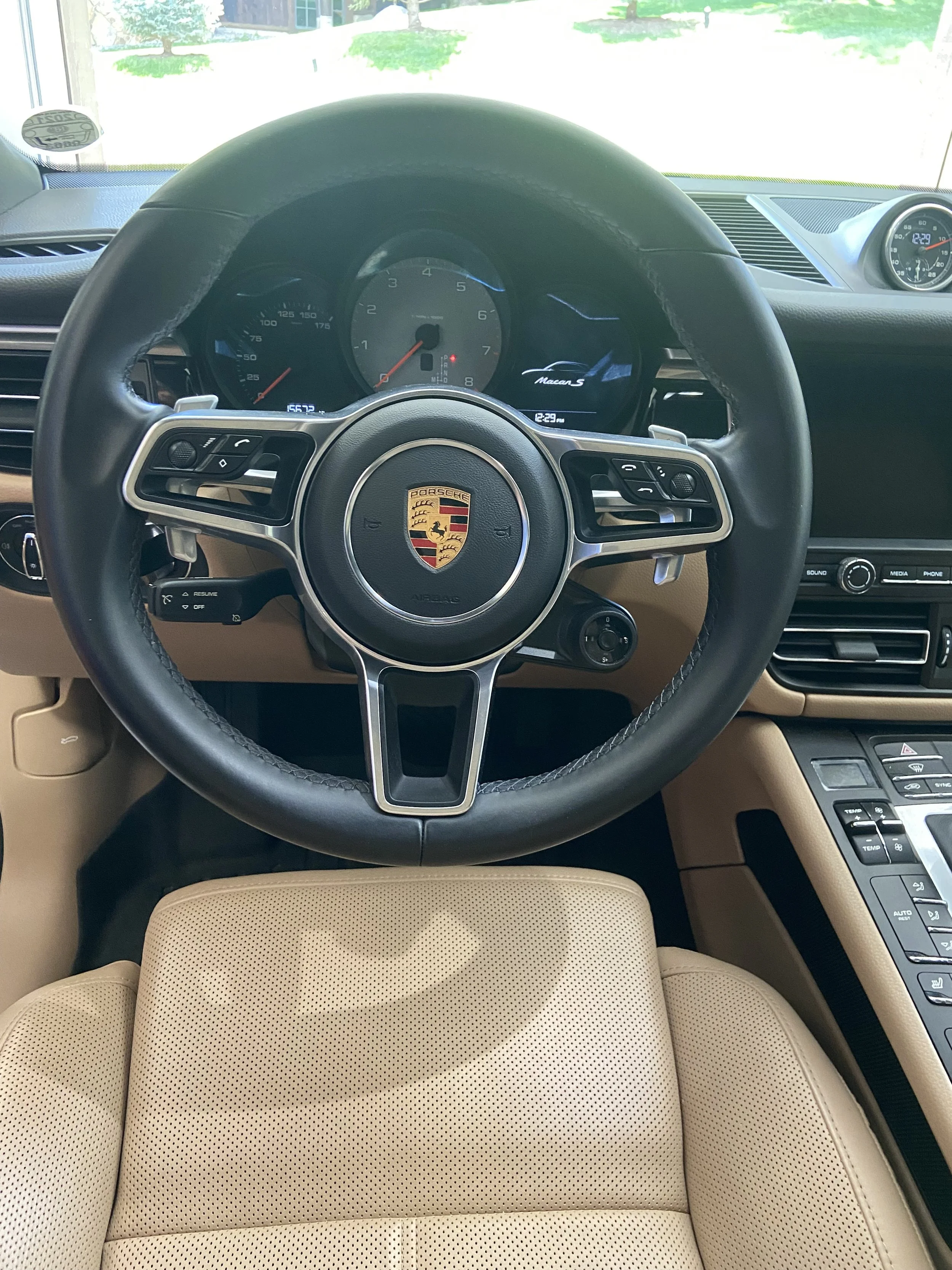 Interior view of a Porsche car, showing the steering wheel with the Porsche logo, dashboard with gauges, a tan leather seat, and dashboard controls.