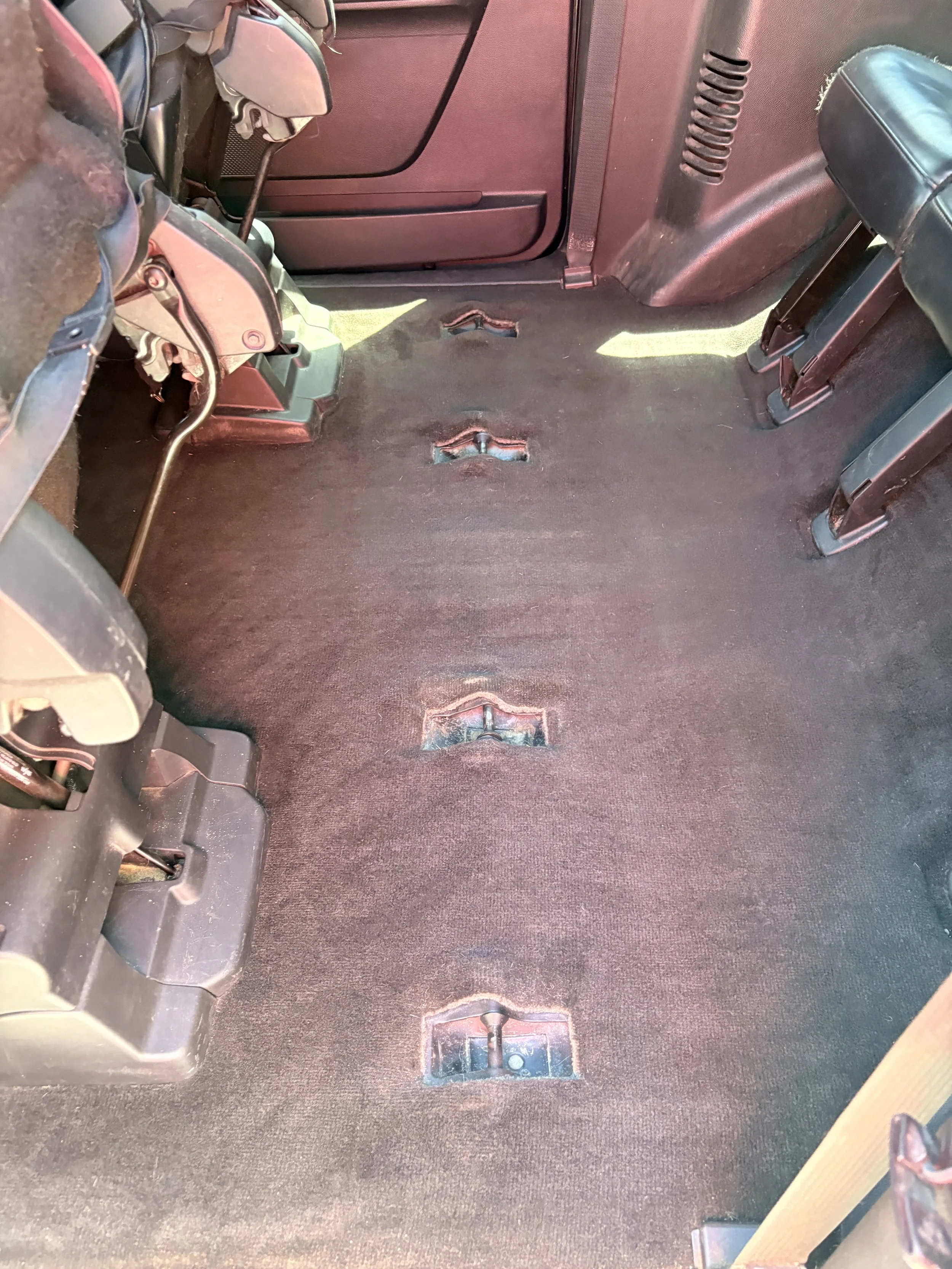 The interior of a vehicle with the seats removed, showing the carpeted floor with four mounting brackets for the seats.