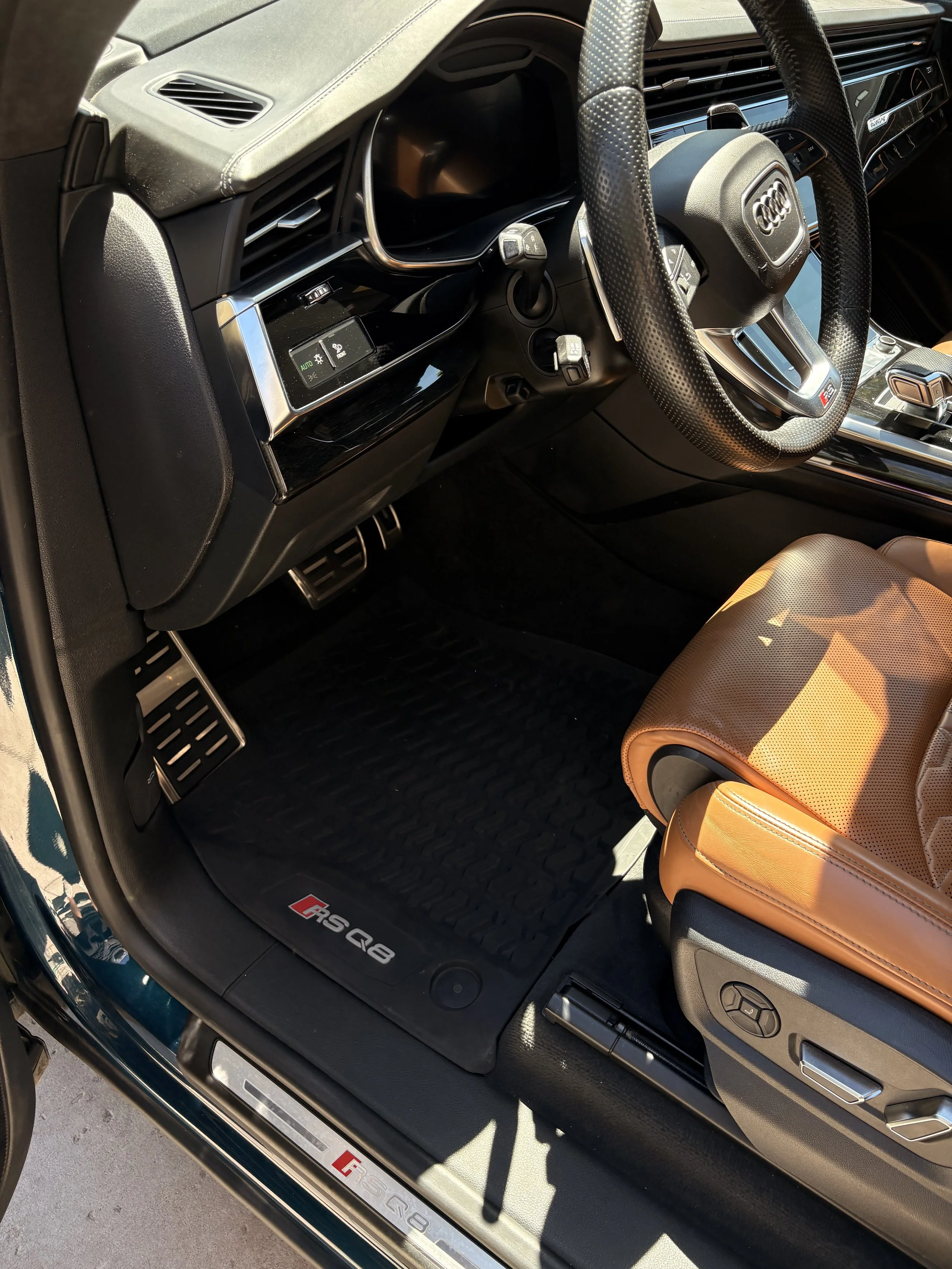 Interior of an Audi RS Q8 sports SUV, featuring a leather-wrapped steering wheel with the Audi logo, digital display, black dashboard, tan leather seat, and metallic accents.