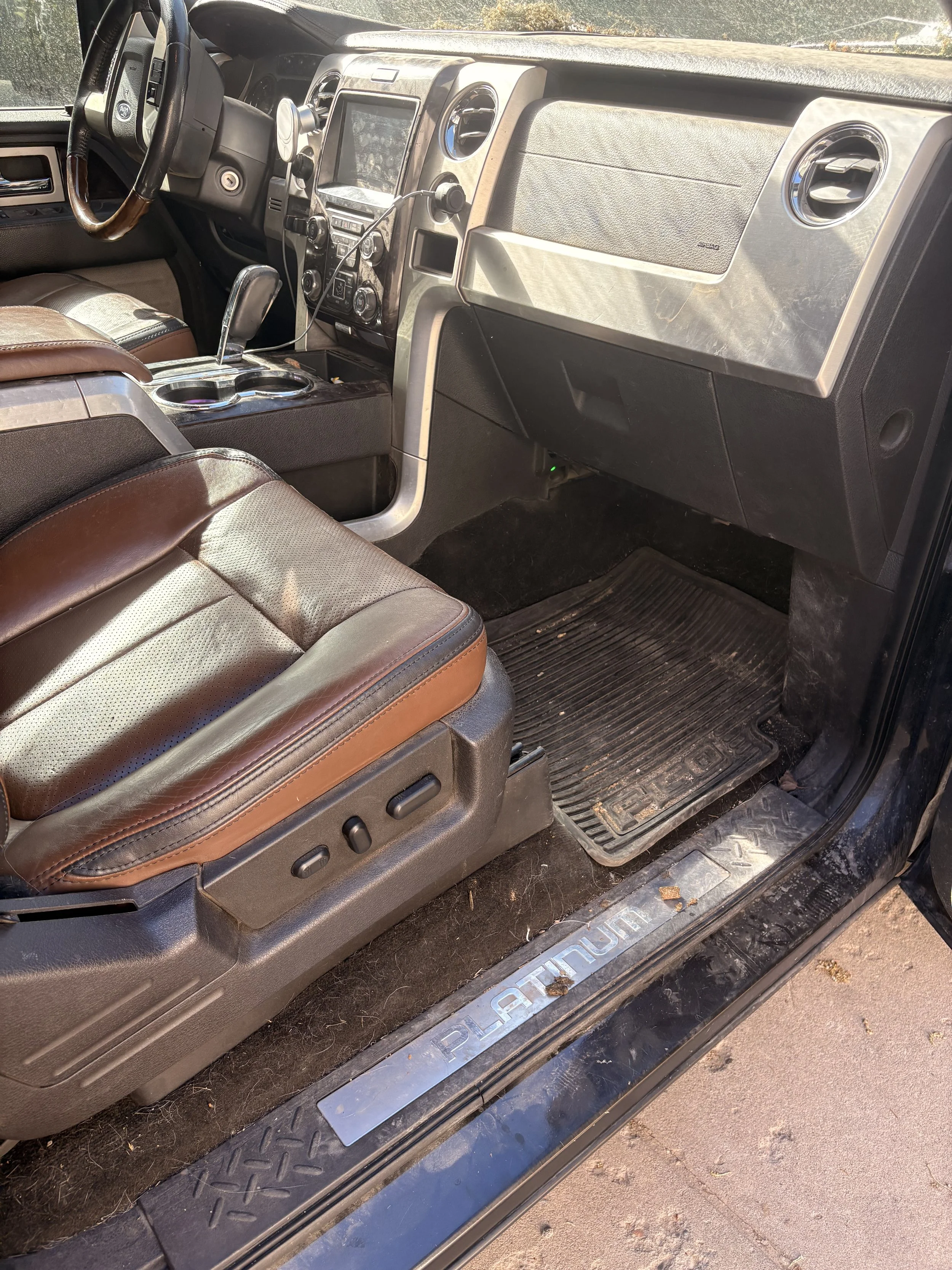 The interior of a vehicle showing the front passenger seat, dashboard, and driver's area, with dirt on the floor and outside view through the windows.