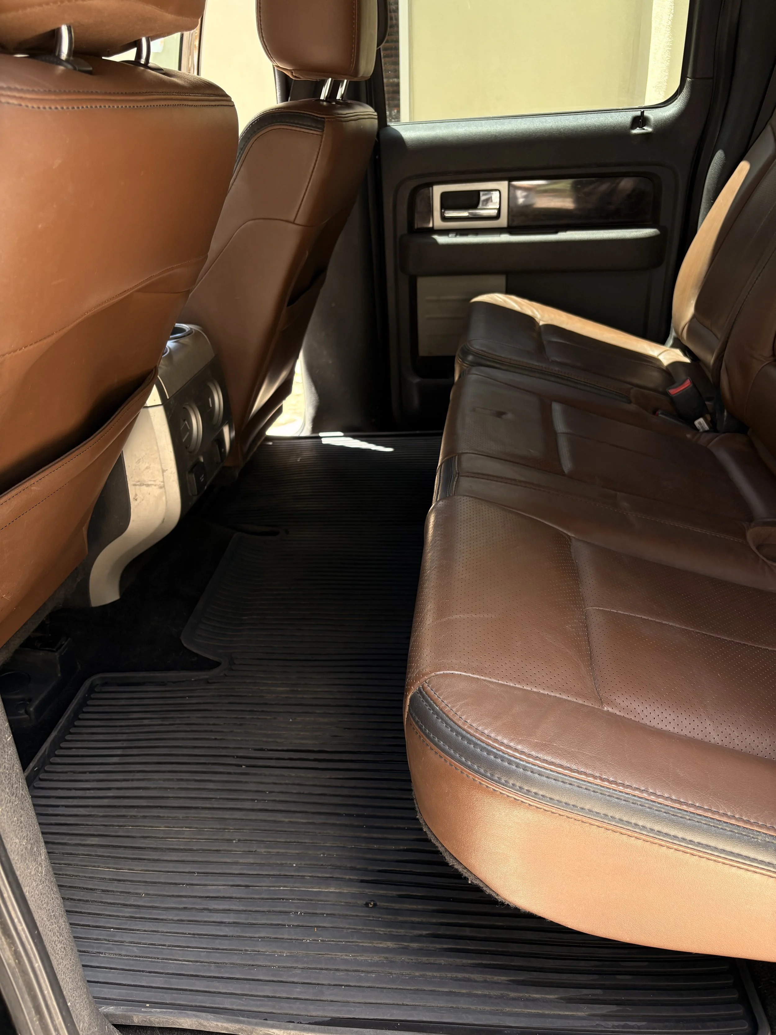 Inside view of a vehicle showing brown leather seats, a black rubber floor mat, and the interior of the passenger door with a window.