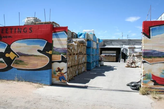 Entrance to a warehouse with colorful graffiti walls, with stacks of building materials and pallets inside under a blue sky.