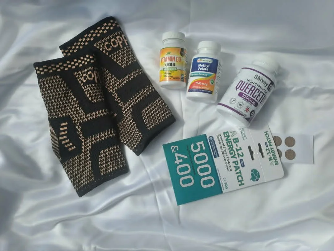 Sports health items including a pair of black and beige toe socks, vitamin D supplement, methylfolate supplement, quercetin supplement, and a high-energy patch, all placed on a white fabric background.