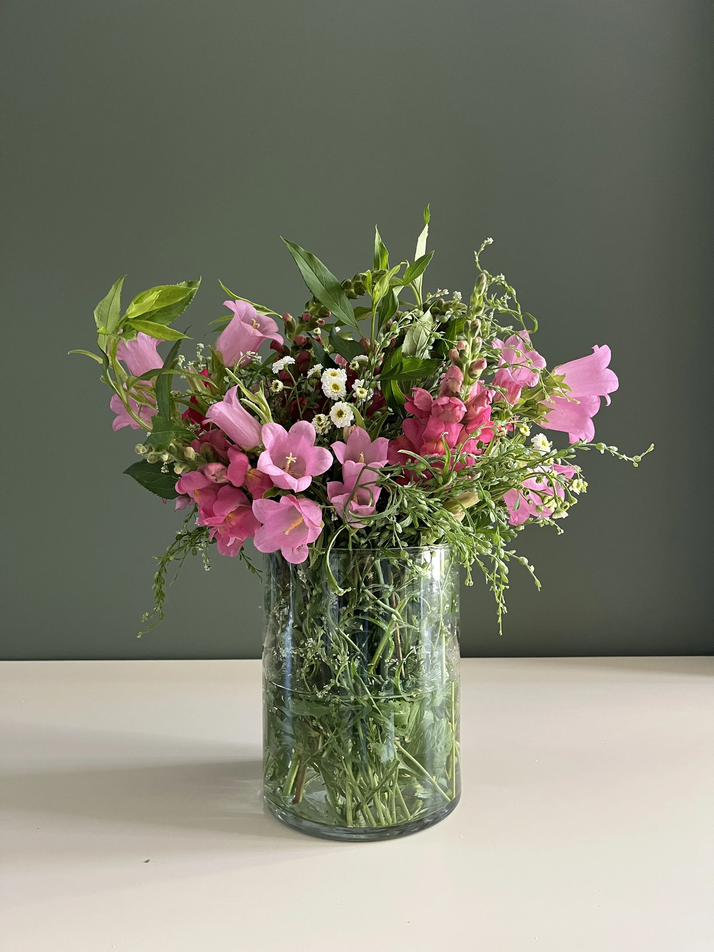 A glass vase filled with pink, white, and green flowers, placed on a white surface against a gray background.