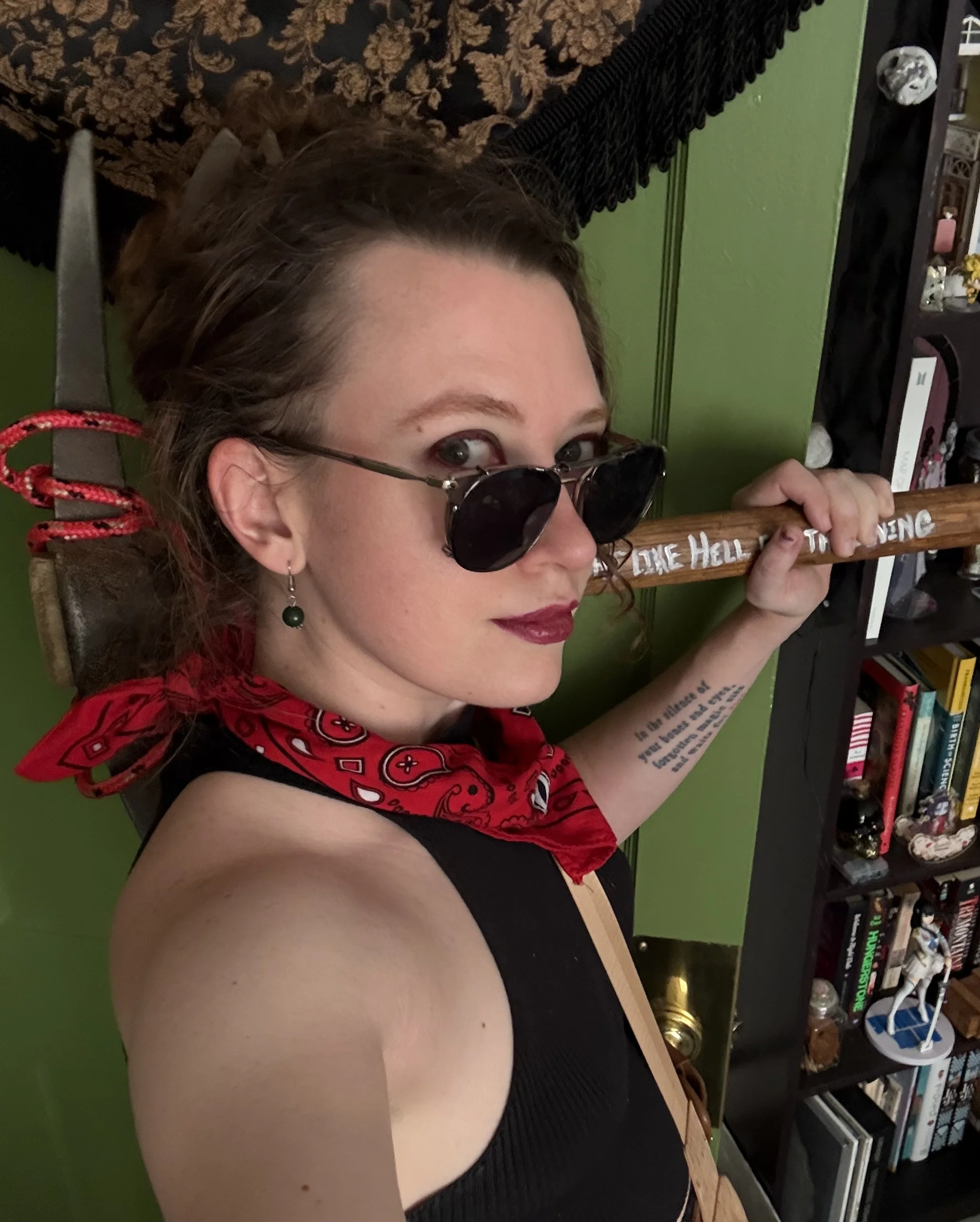 Paige Reiring faces right while looking at the camera. She wears a red bandana and has a pickaxe on her shoulder.