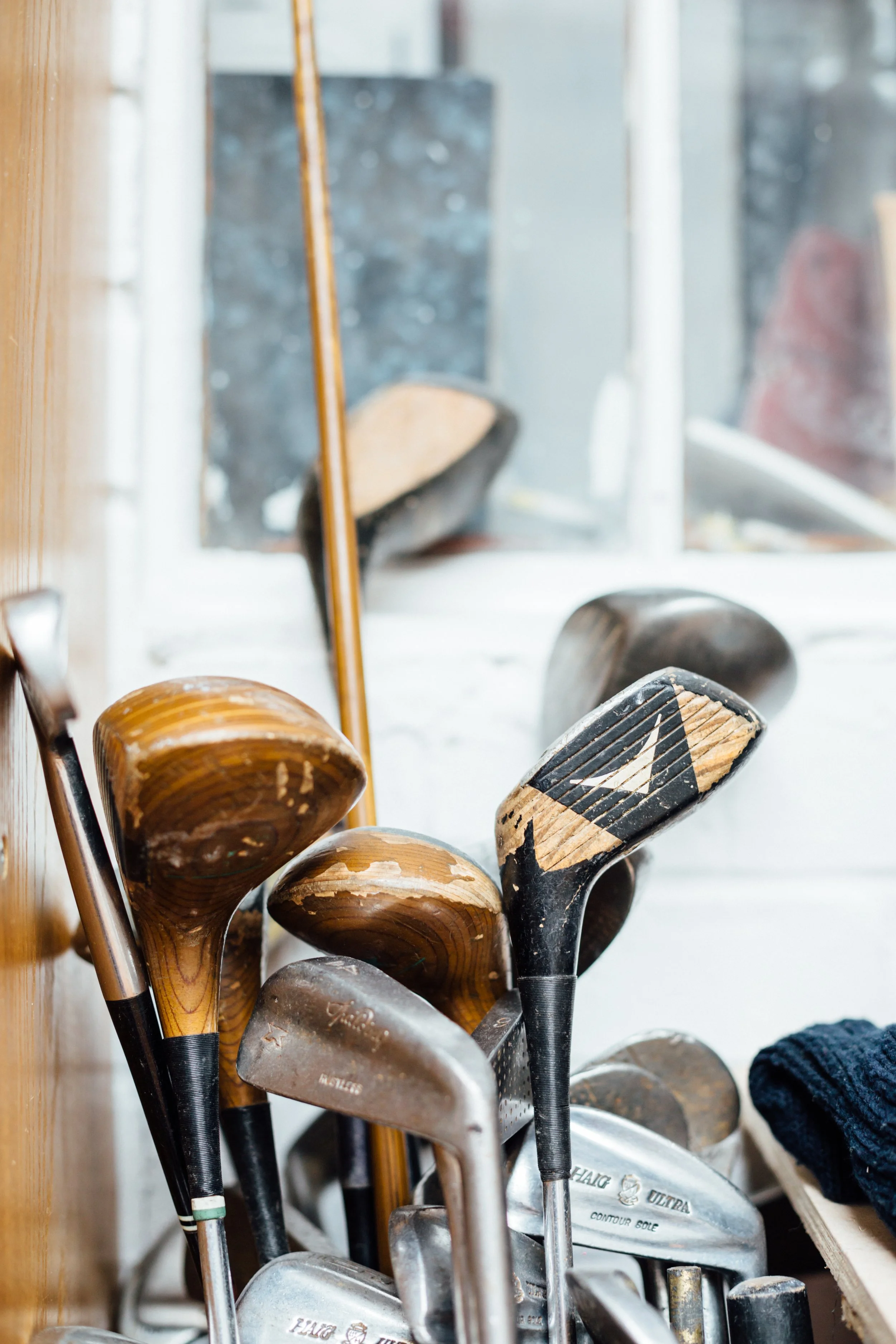A collection of golf clubs with wooden, metal, and graphite shafts, leaning against a wall or stand.