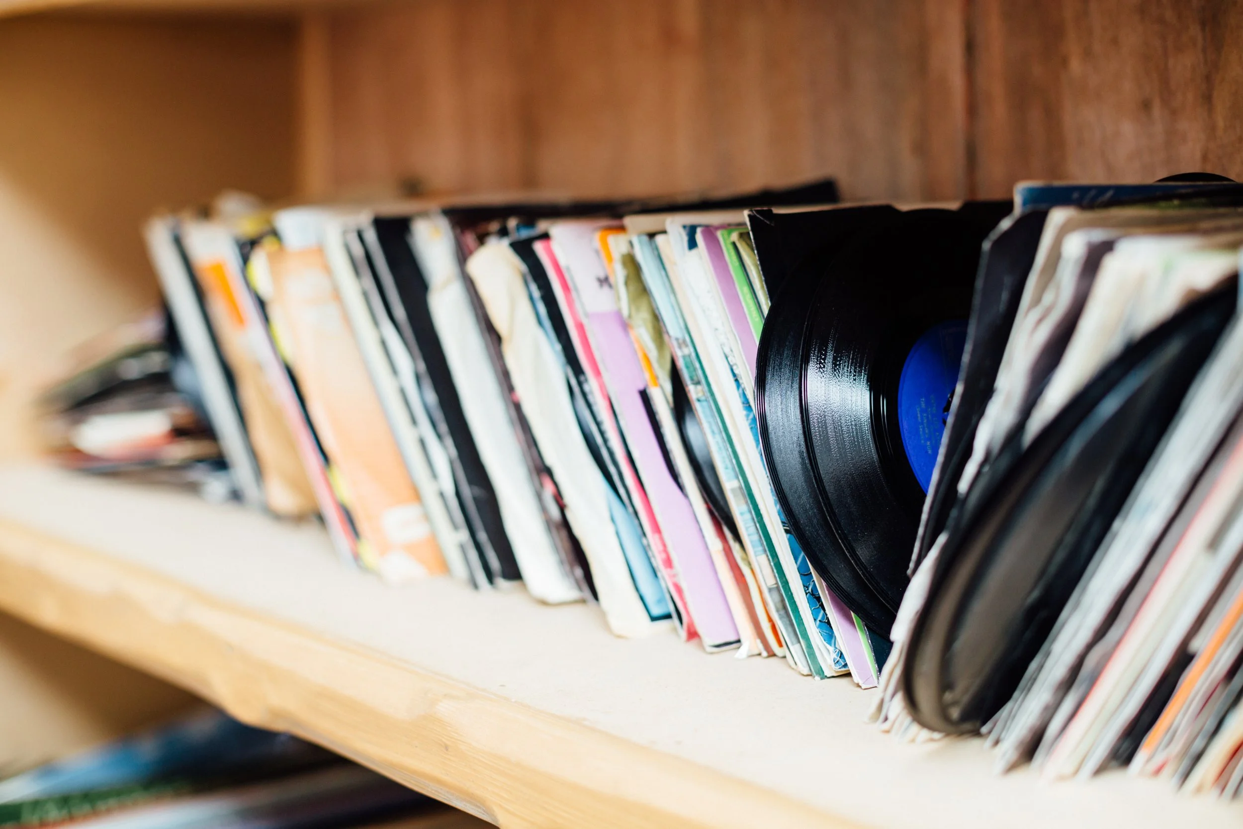 A bookshelf filled with an assortment of books and vinyl records, some with visible colorful spines and covers.