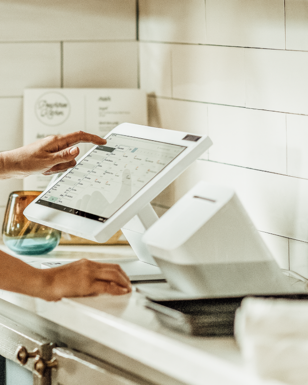 Hands using a touchscreen point of sale system at a restaurant counter.