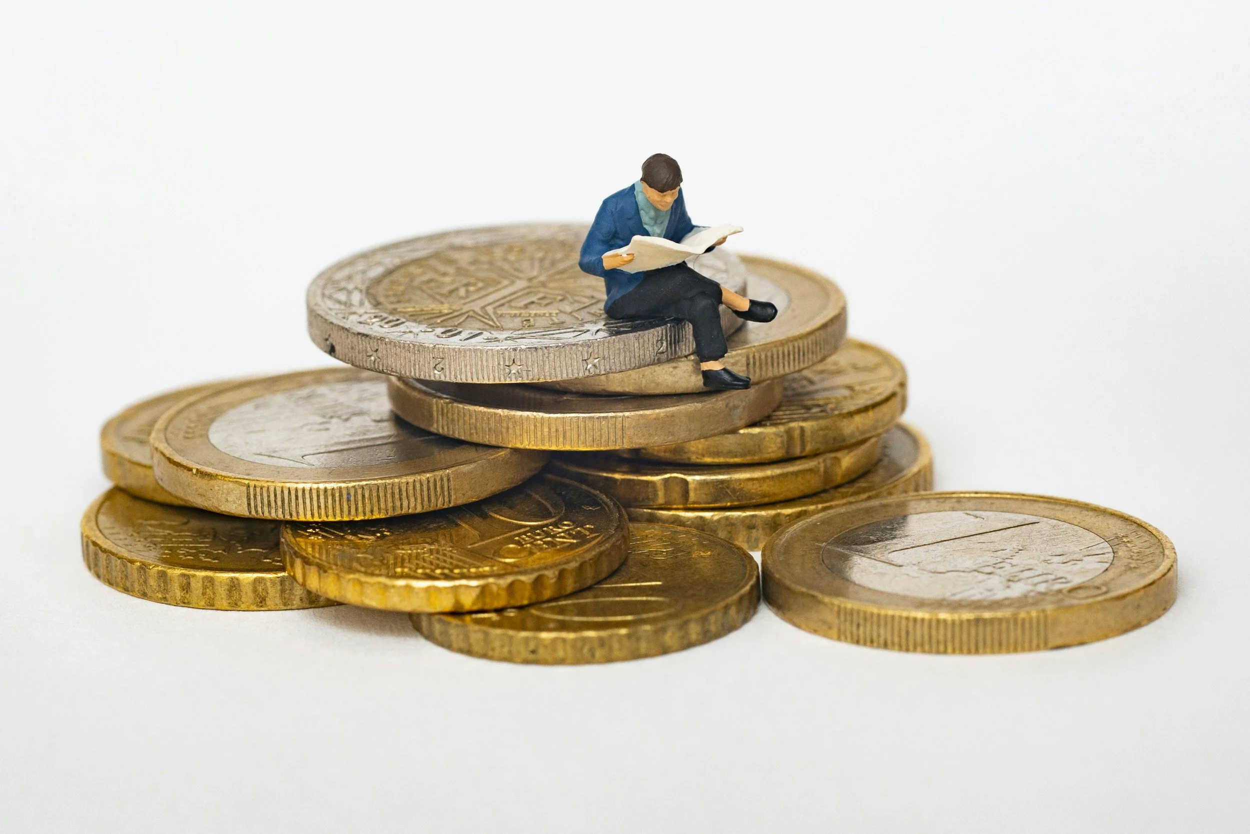 Miniature figure of a man sitting on top of a stack of coins, reading a newspaper.