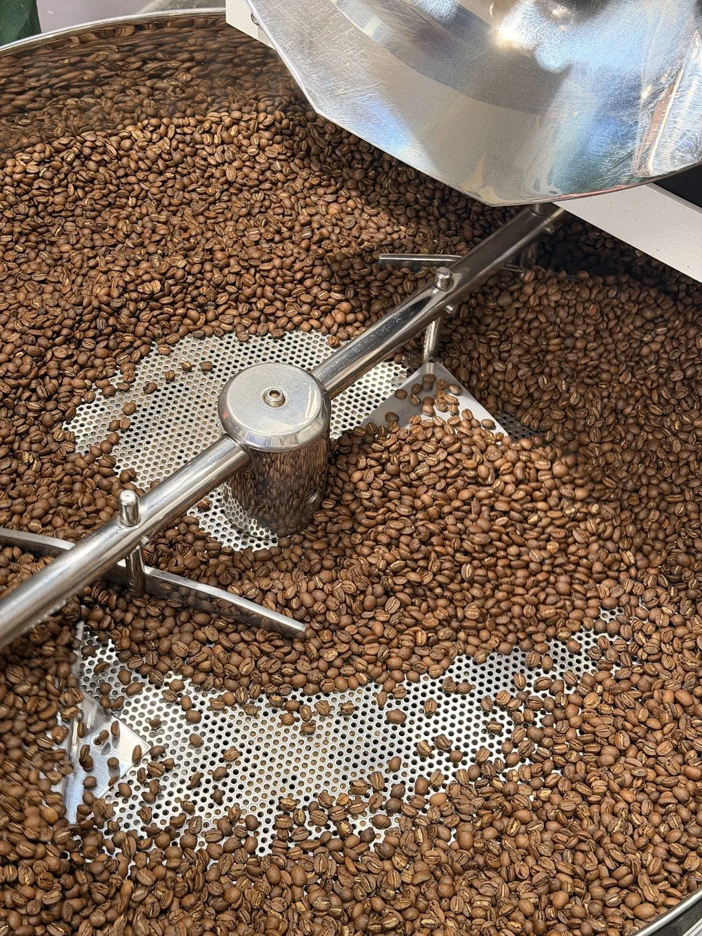 Close-up of a coffee roasting machine with roasted coffee beans inside, metal components, and a perforated surface.