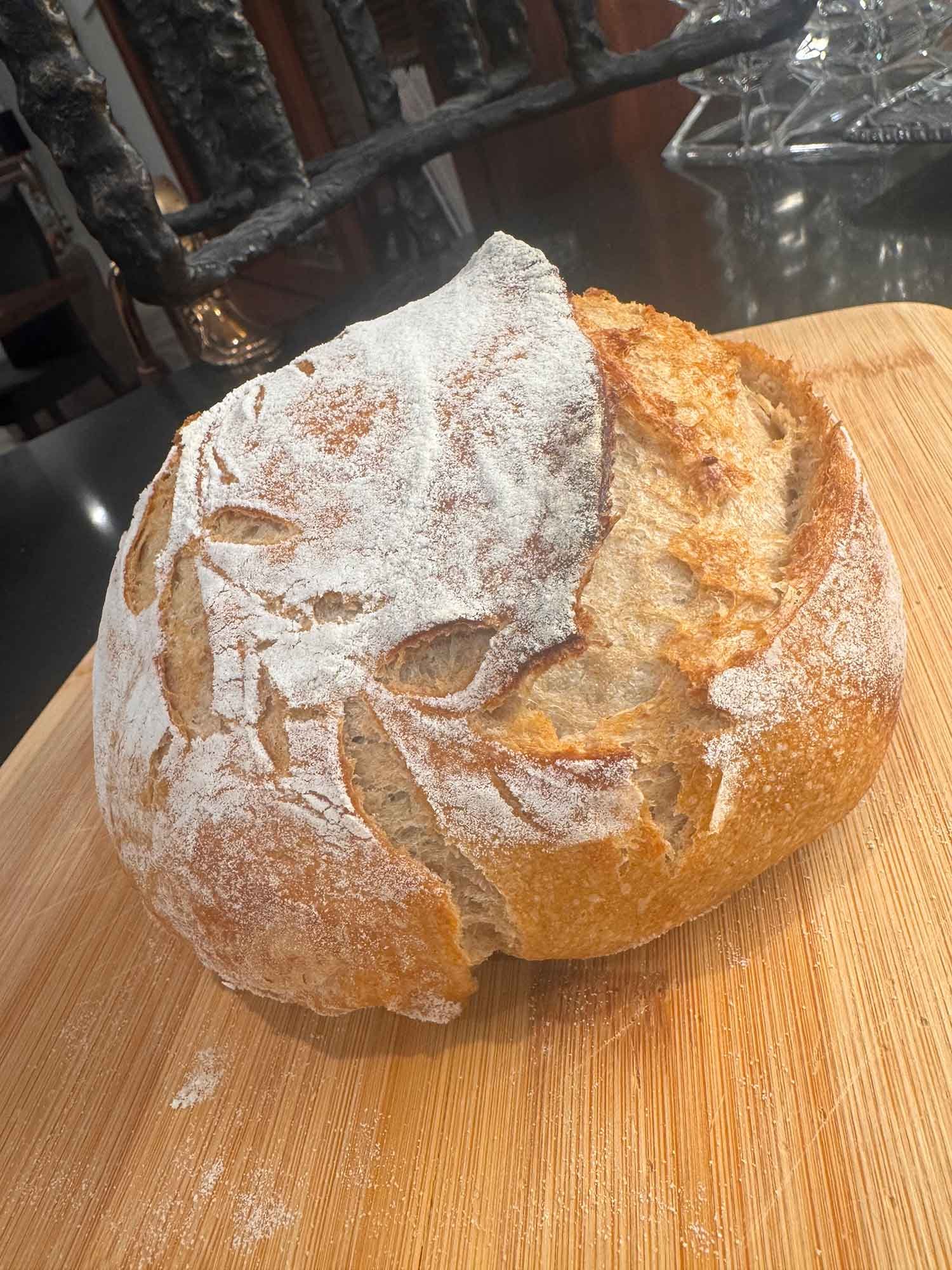 A loaf of bread dusted with flour, placed on a wooden cutting board.