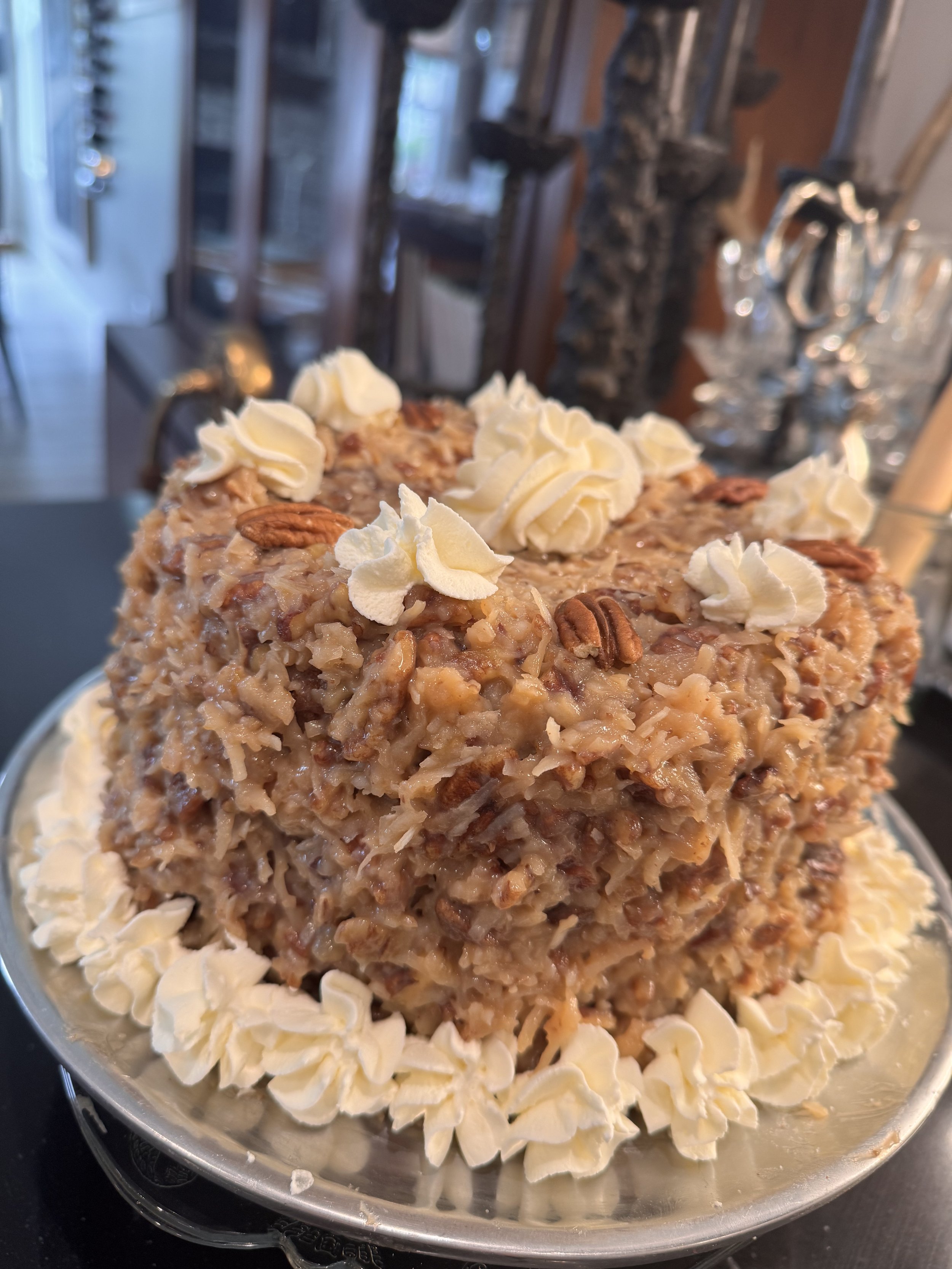 A close-up of a dessert topped with whipped cream and pecans, surrounded by sliced almonds, on a silver platter.