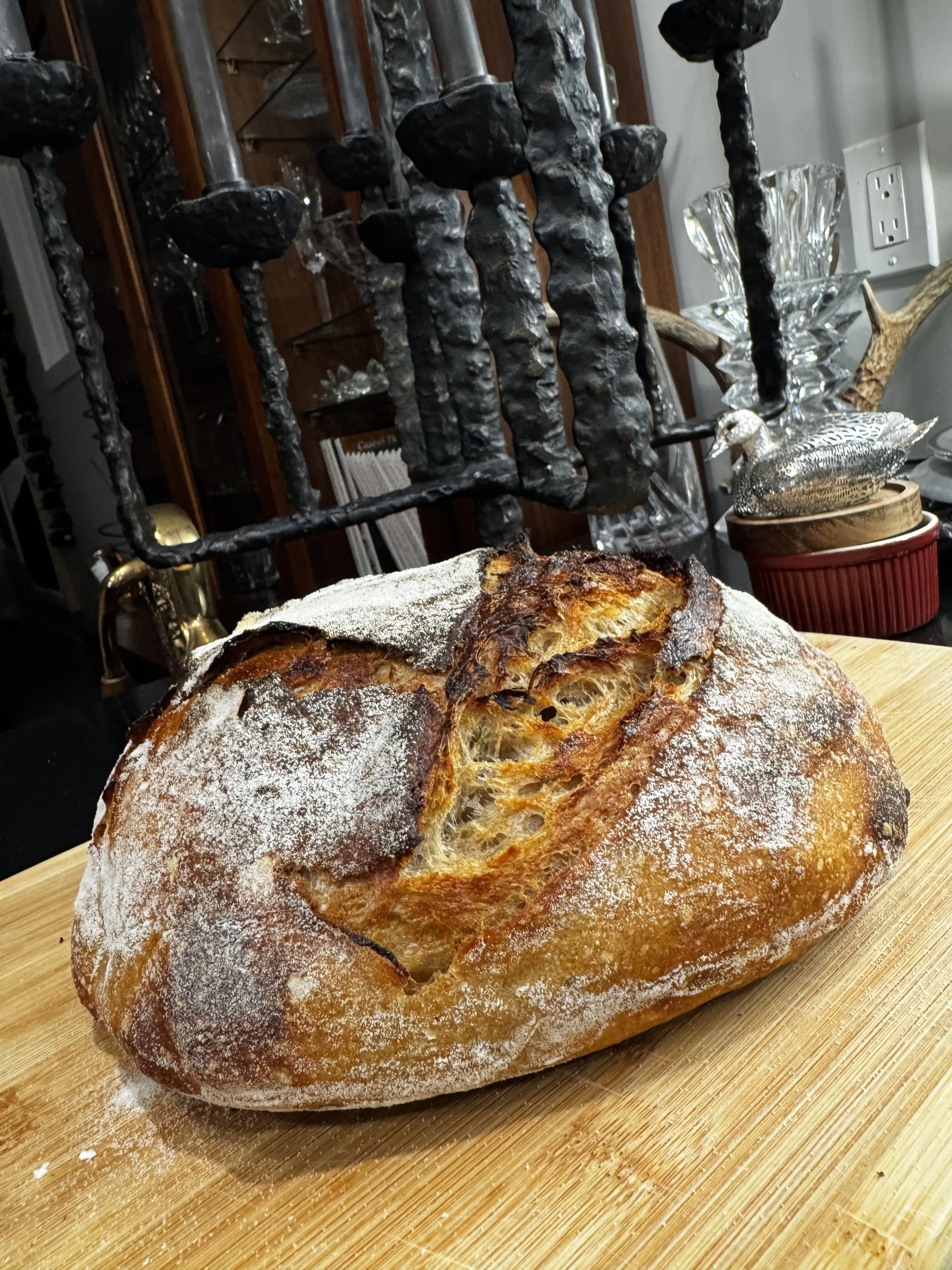 Freshly baked round loaf of bread with a crispy crust and dusted with flour, placed on a wooden cutting board.