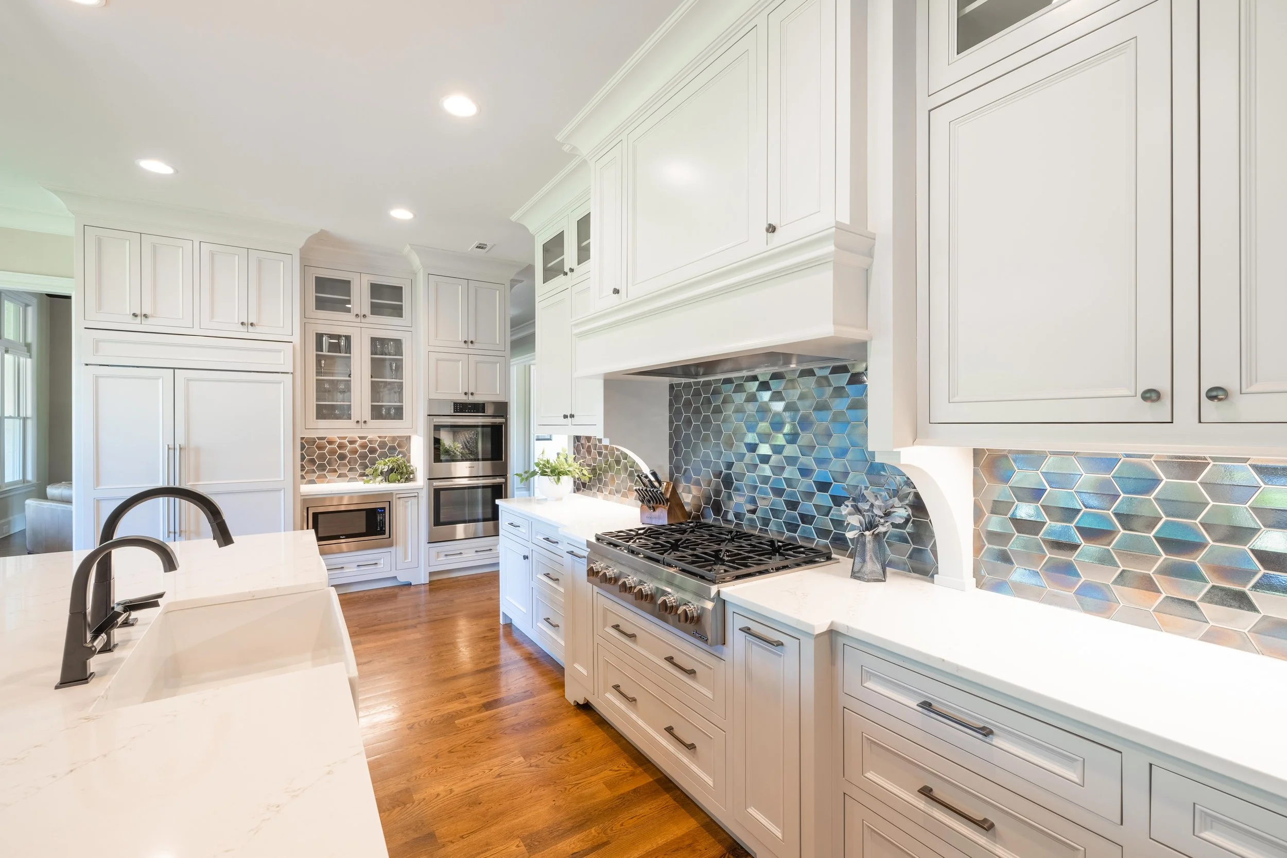 White kitchen with wooden floors, cabinets, a stove with a metallic backsplash, and a kitchen island with a white marble countertop.
